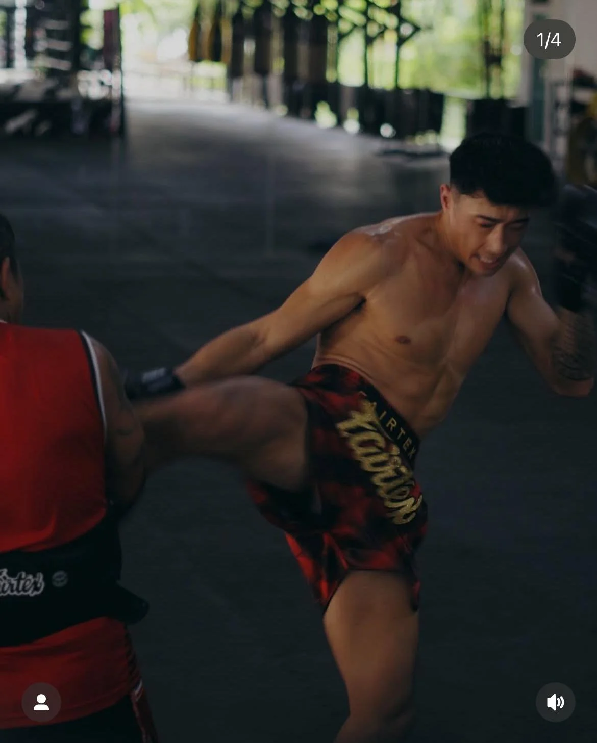 Male martial artist practicing a high kick with a trainer in a gym.