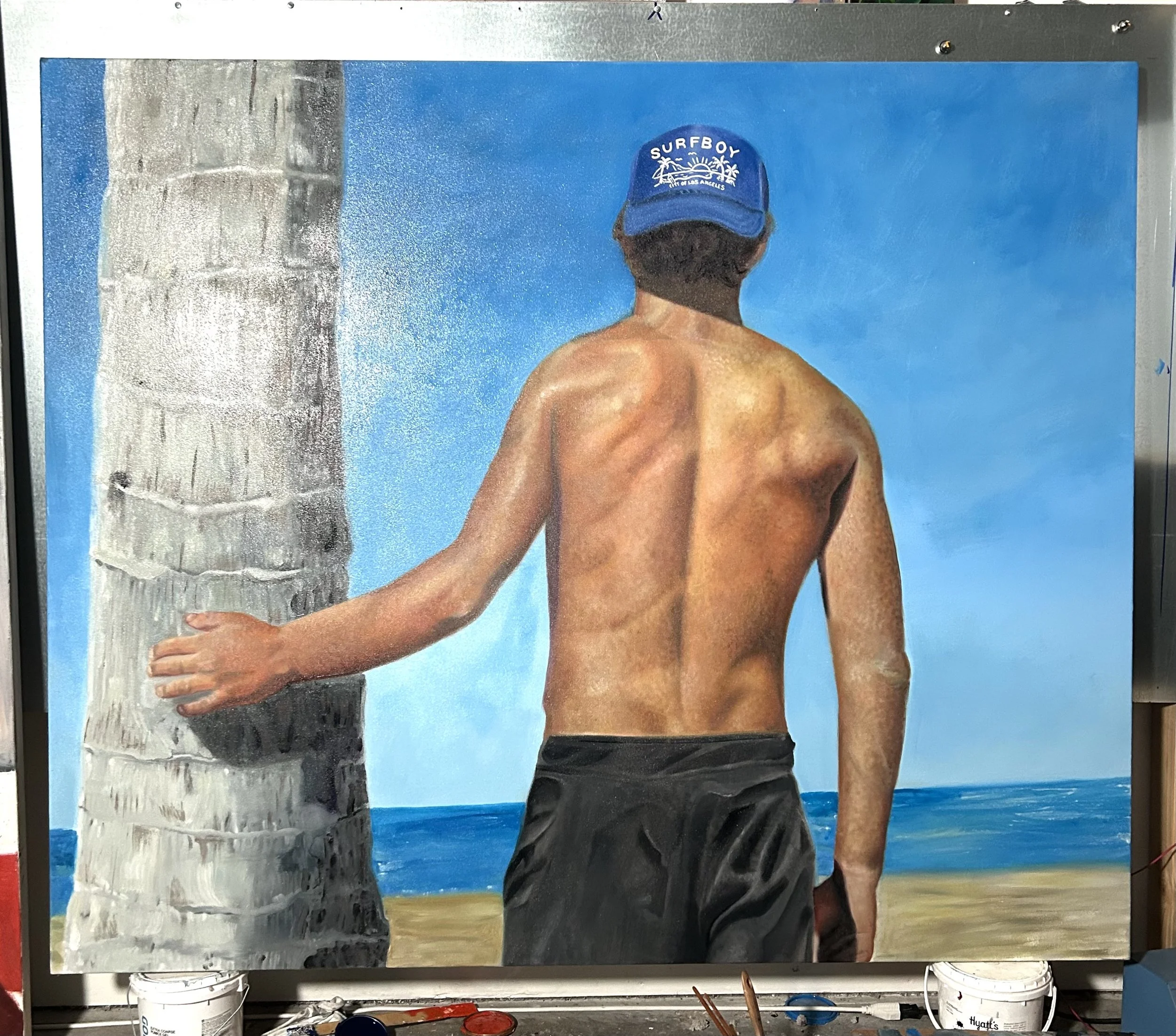 A painting of a shirtless man holding a palm tree trunk, seen from behind, wearing black shorts and a blue cap with 'SURFBOY' written on it, against a beach background with blue sky and ocean.