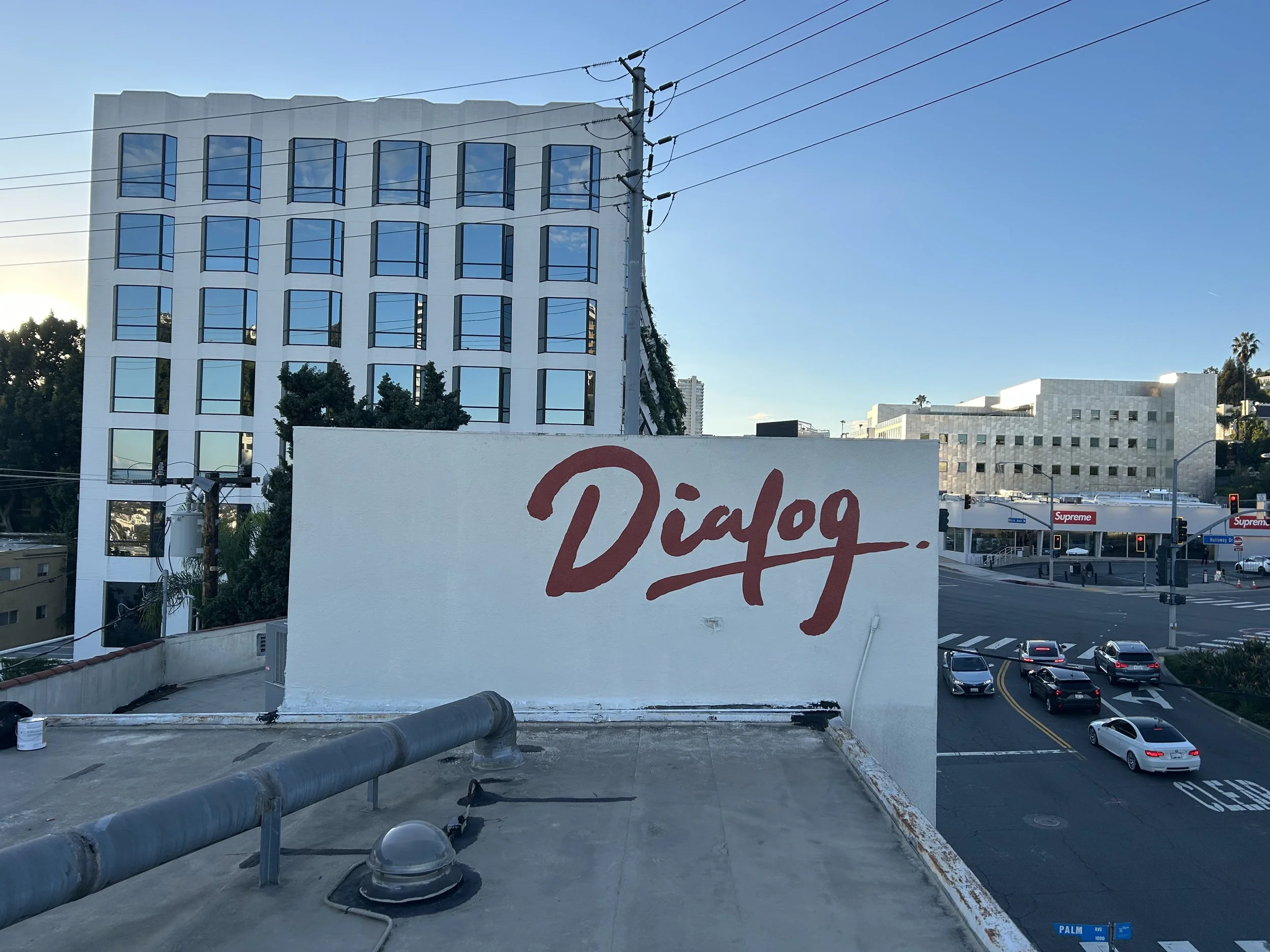 A white wall with red graffiti spelling 'Digg' in front of a cityscape with modern buildings, cars, and utility poles under a blue sky.