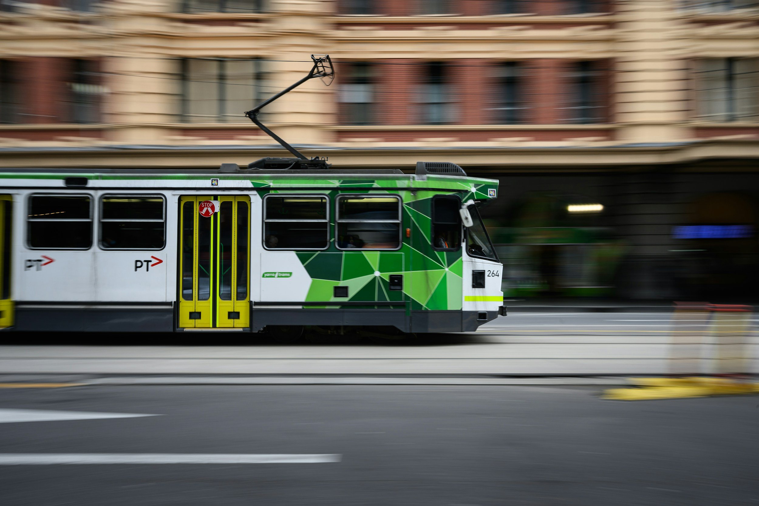 An urban tram moving quickly on tracks in a city street with blurred buildings in the background.