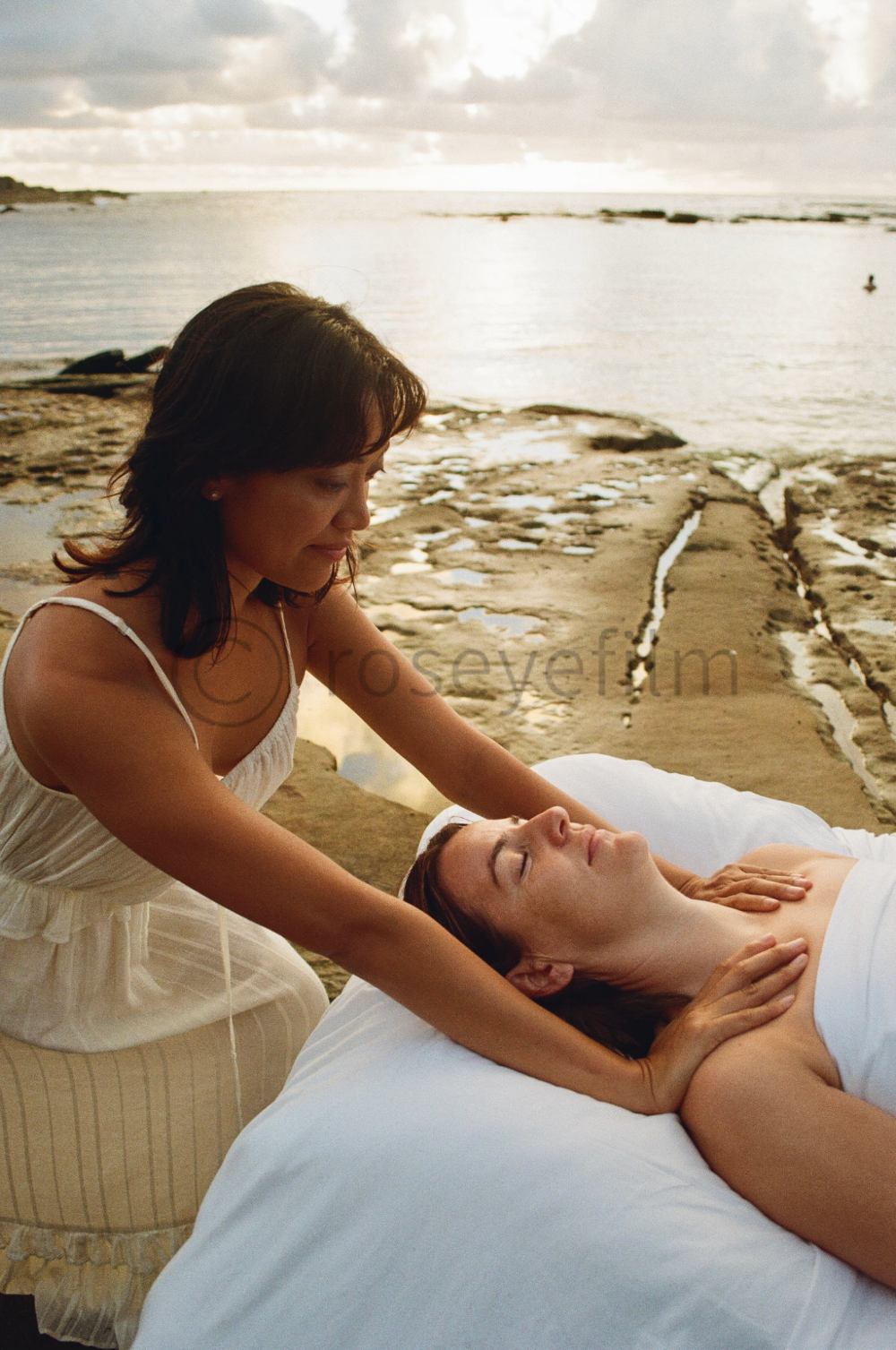 A woman receiving a massage on a beach at sunset, with the ocean in the background.
