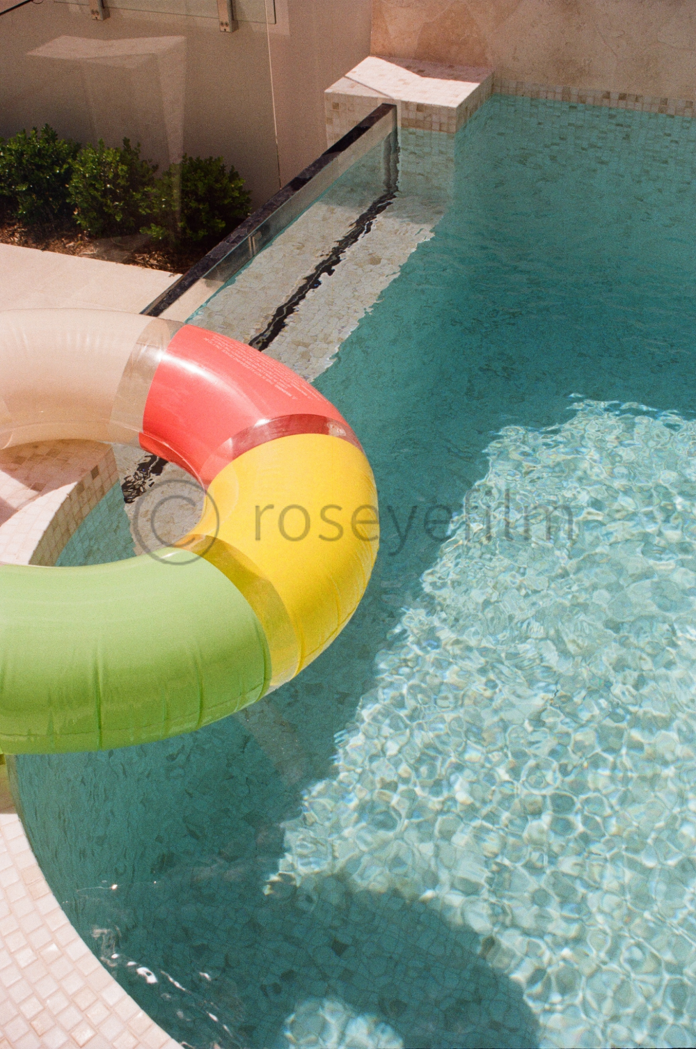 Swimming pool with a colorful water slide, featuring sections in red, yellow, and green, and clear water with a tiled surface underneath.