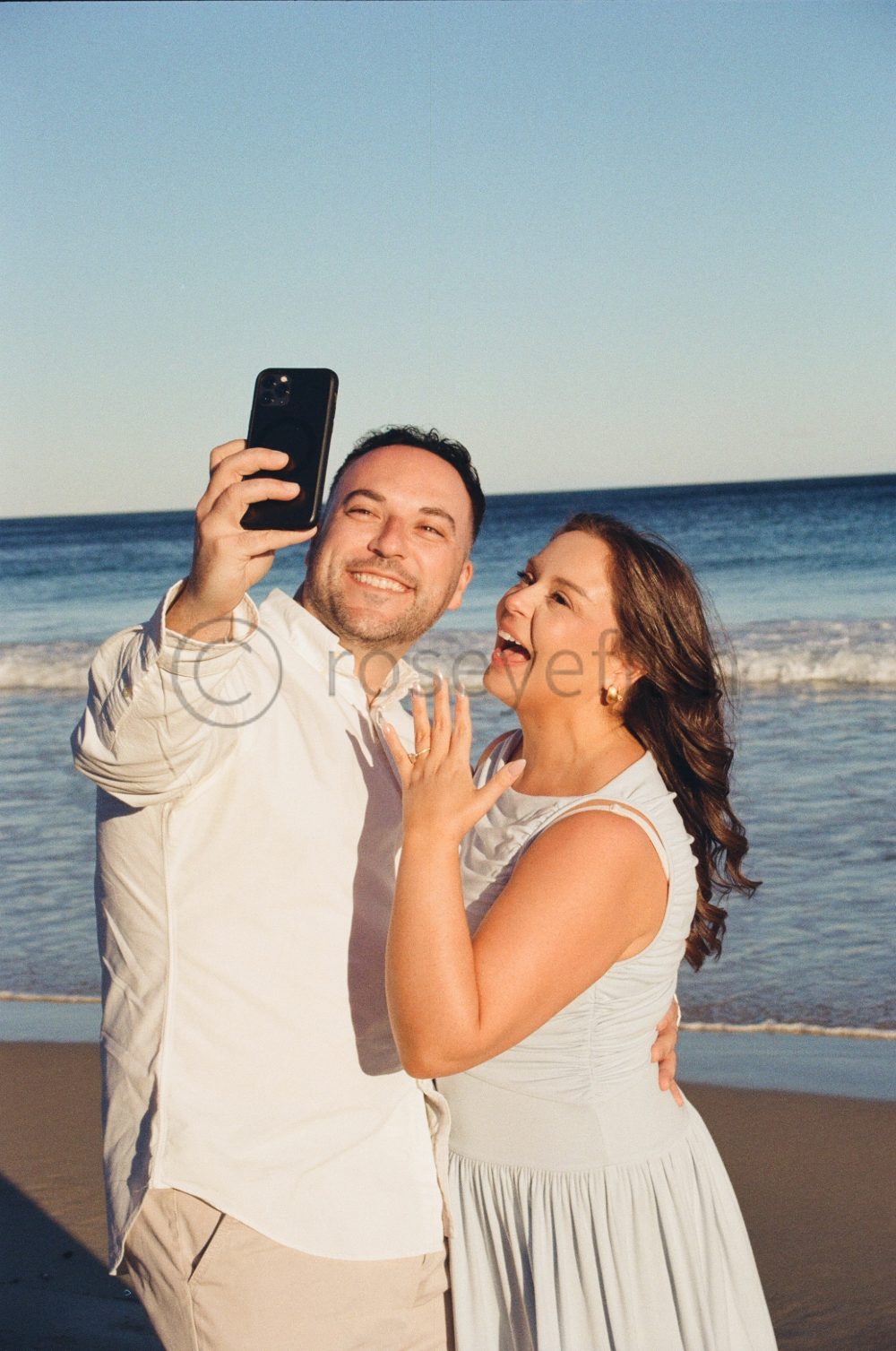 A happy couple taking a selfie on the beach during sunset.