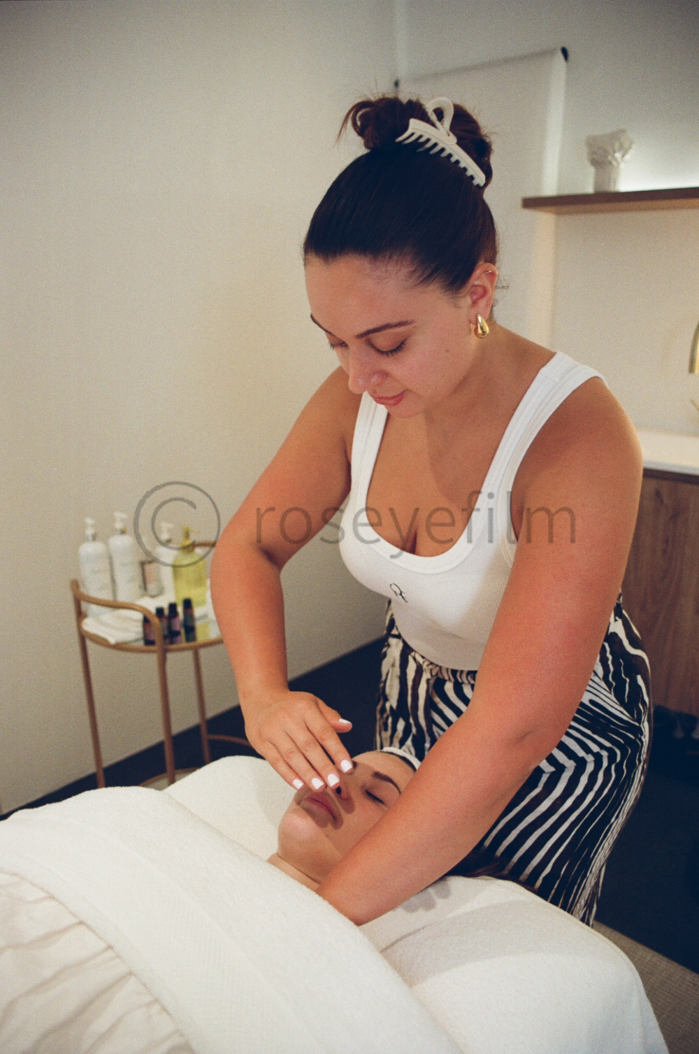 A woman giving a facial massage or treatment to a woman lying on a massage table in a spa or treatment room.