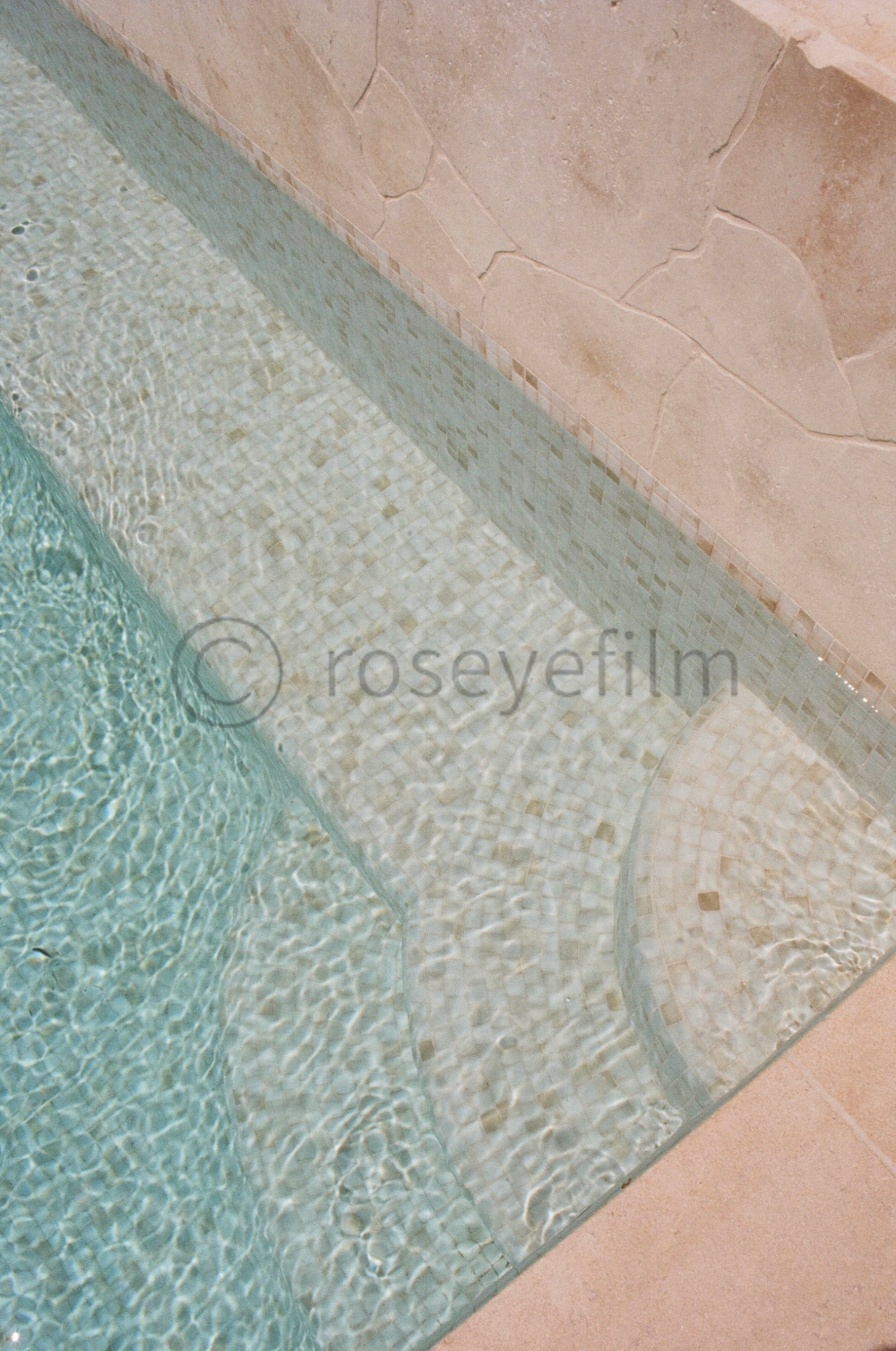 Close-up of a swimming pool corner with tiled edge and beige stone wall.
