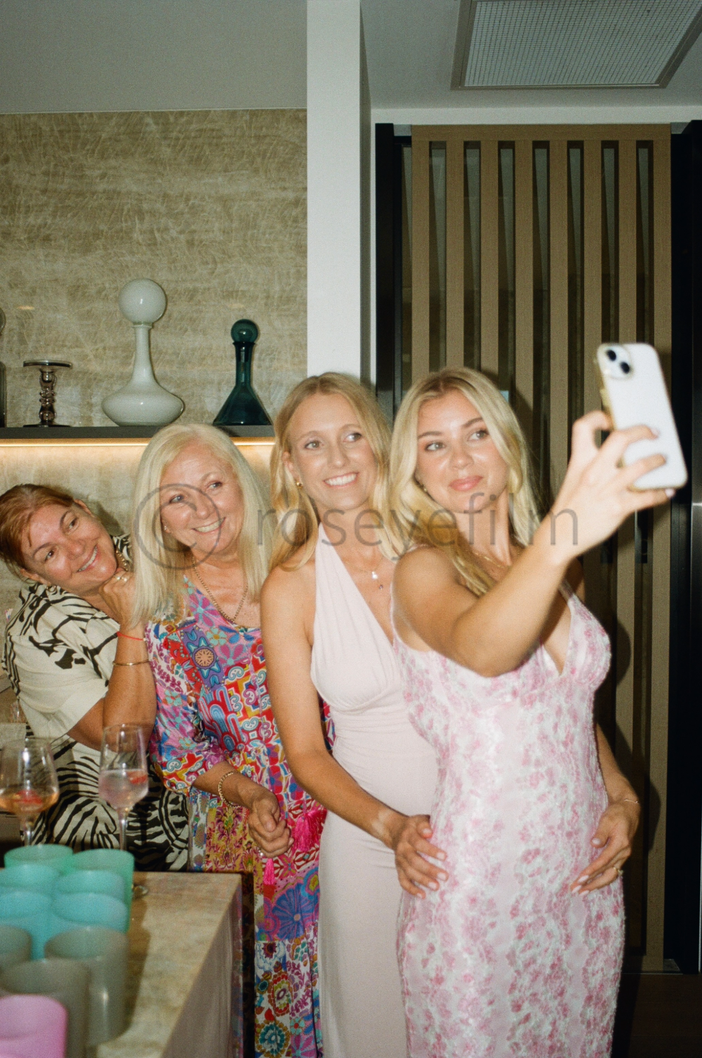 Four women taking a selfie together at a social gathering, smiling and posing for the camera.