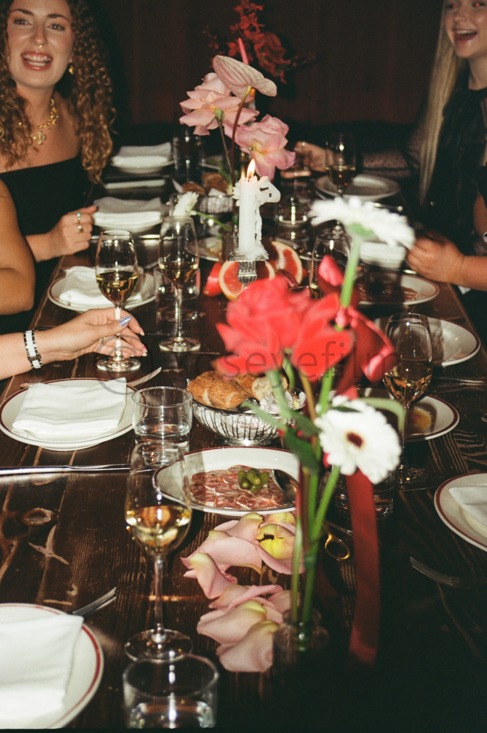 People sitting around a decorated dining table with flowers, wine glasses, and various dishes, celebrating a special occasion.