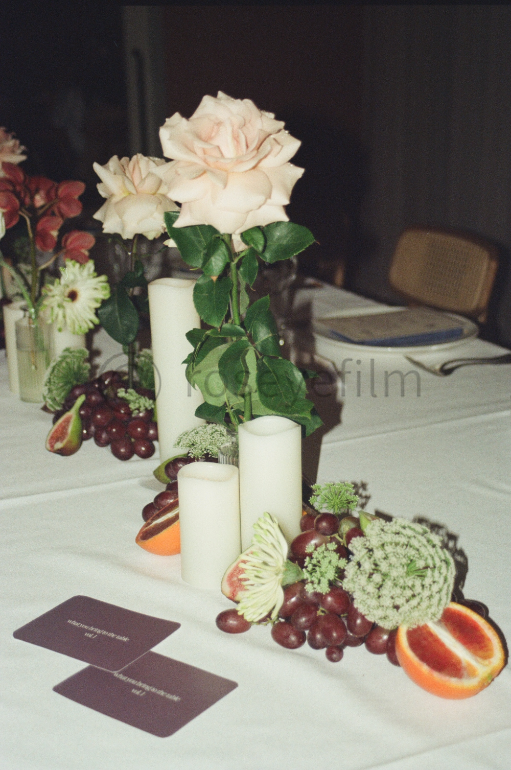A table decorated with pink roses, various grapes, blood oranges, and white candles in a floral arrangement.