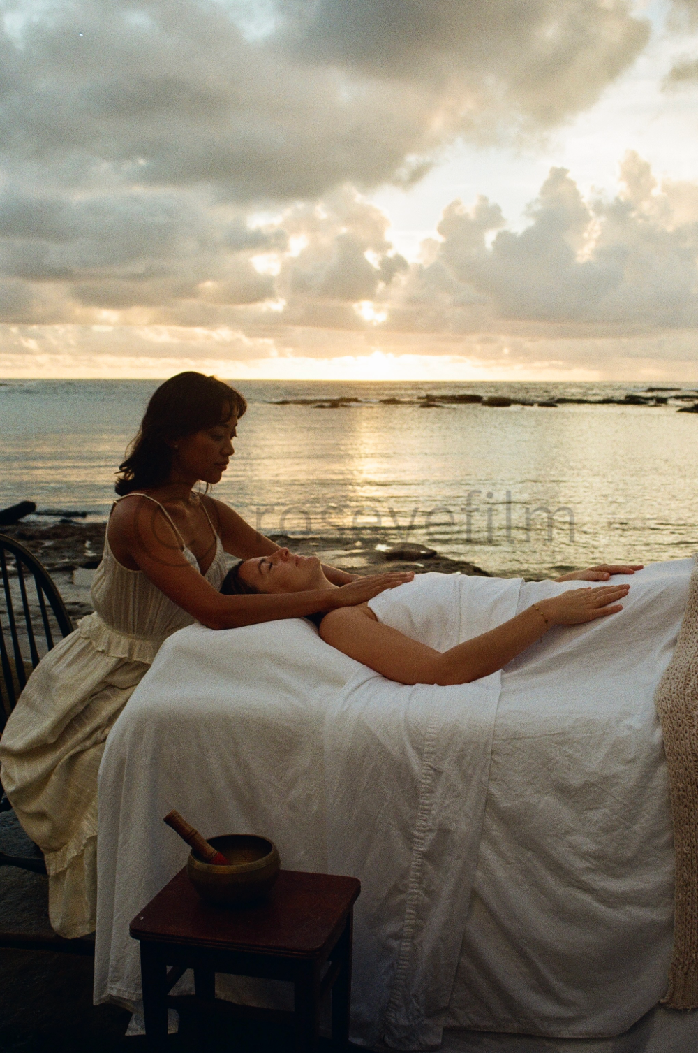 A woman receiving a massage outdoors by the water during sunset.