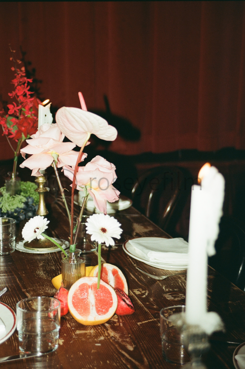 A decorated dining table with pink and white flowers, candles, and sliced grapefruit in the center.