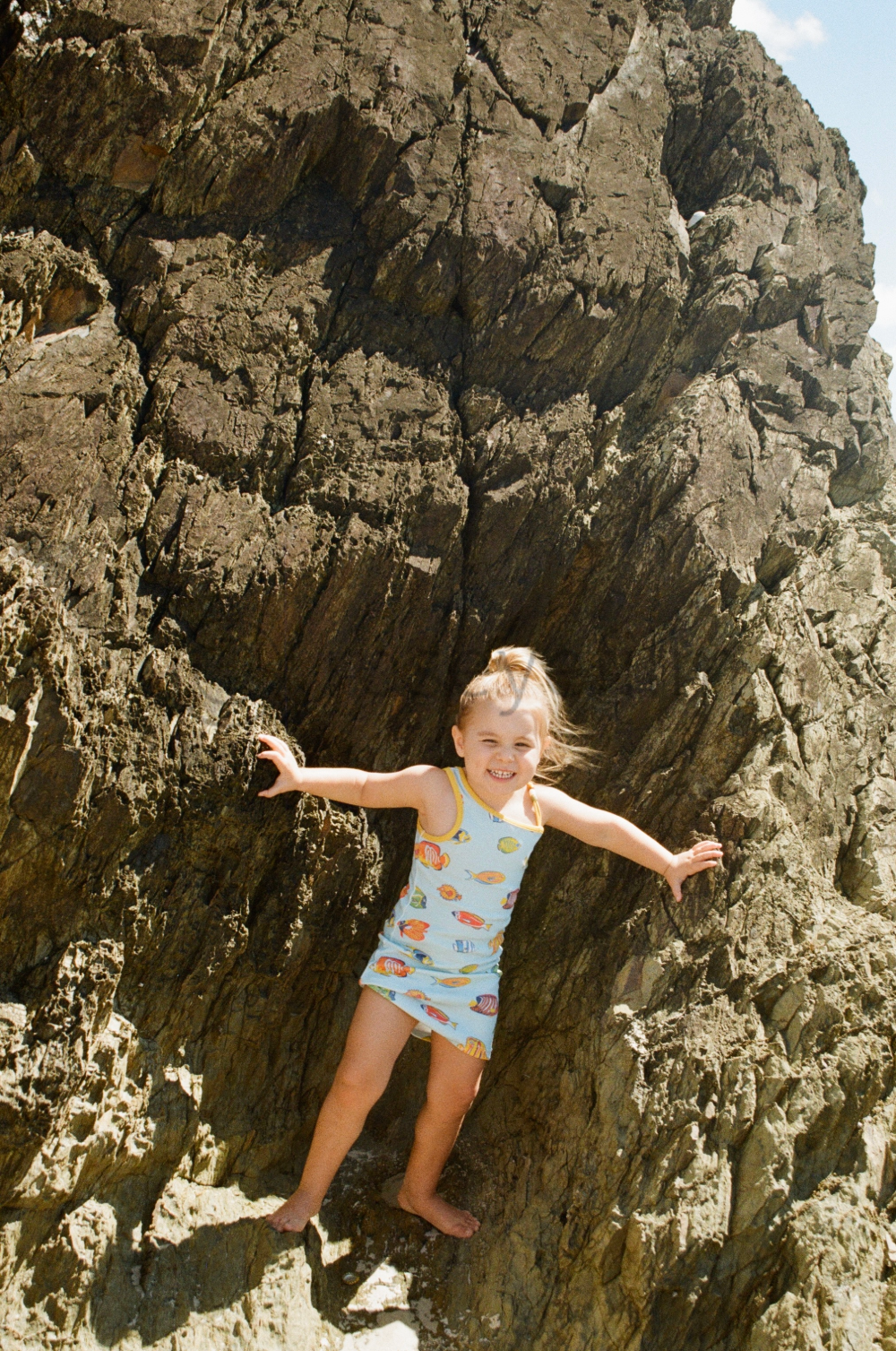 A young girl in a colorful swimsuit climbing and balancing on rocky terrain outdoors during daytime.