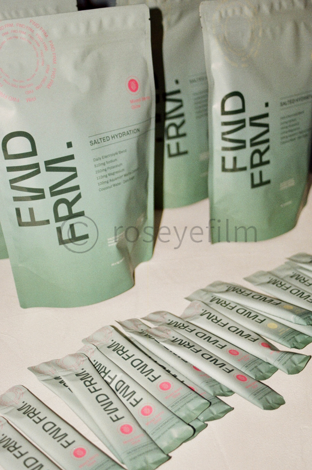 Multiple light green packet pouches labeled 'FWD FIRML' arranged on a white surface, with two standing upright in the background. The packets are part of a product called 'Salted Hydration' with various ingredients listed.