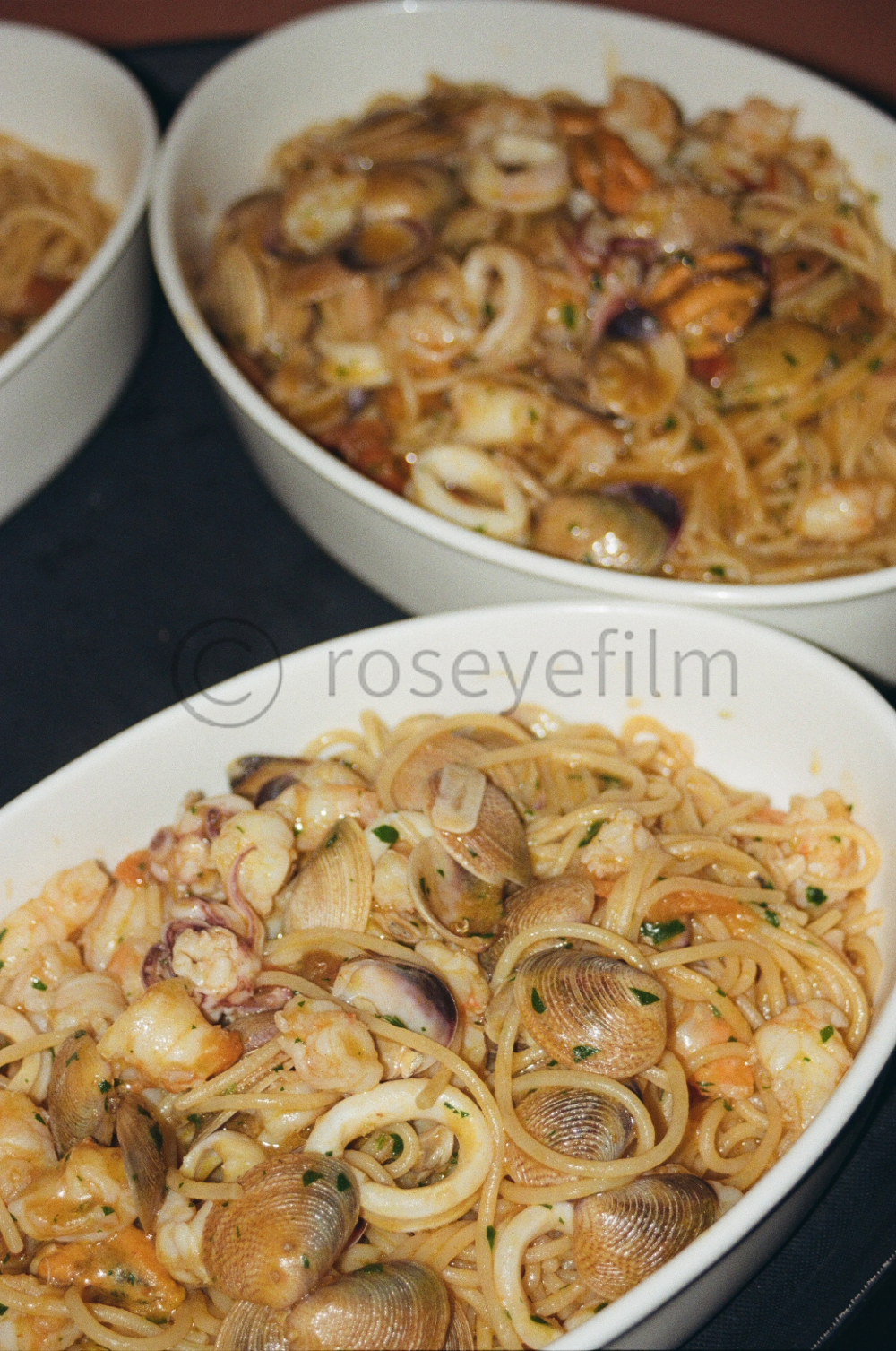 Two white bowls filled with seafood spaghetti, featuring shrimp, clams, and pasta in a tomato-based sauce, topped with chopped parsley.