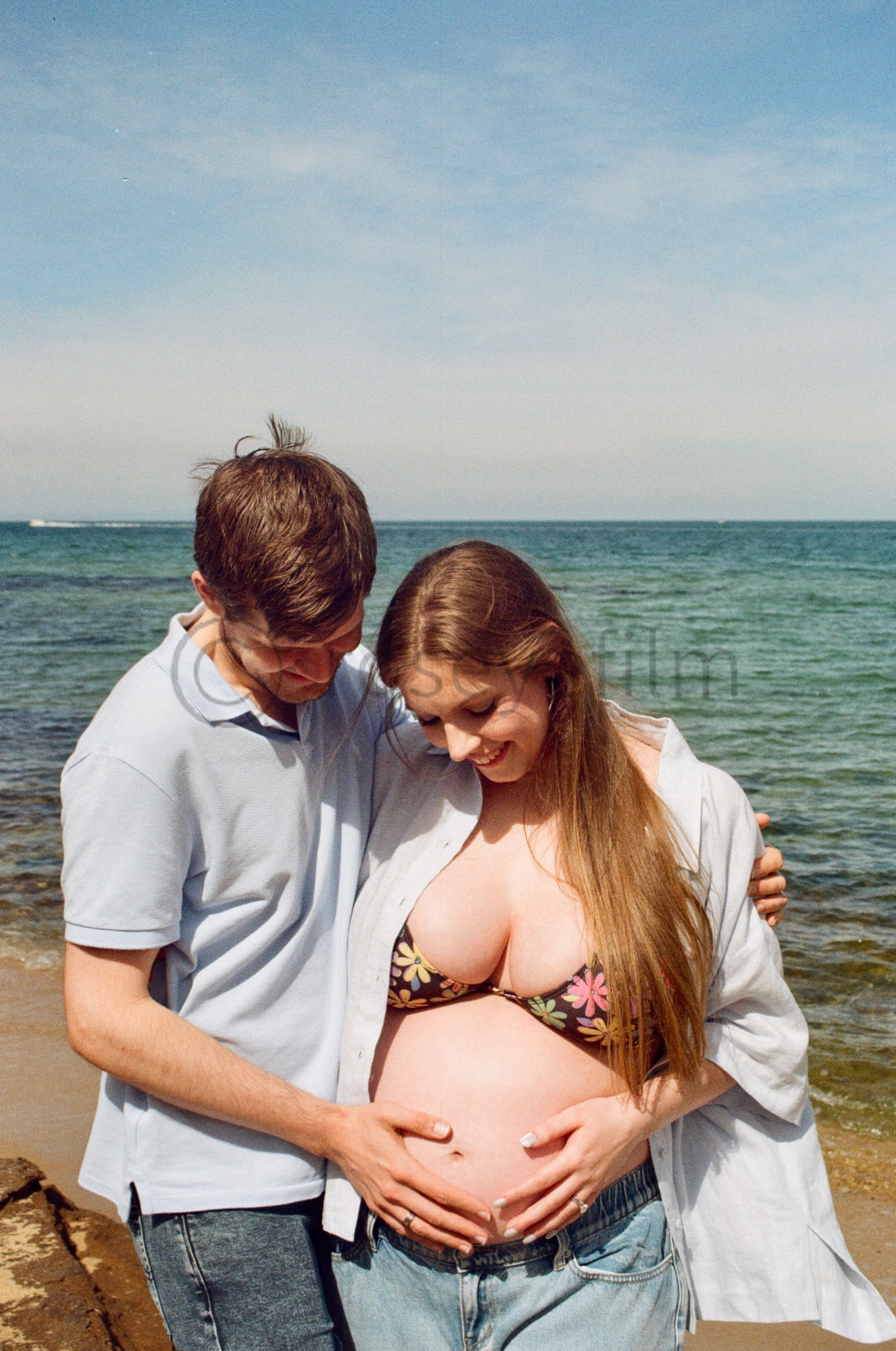 A pregnant woman on a beach with her partner, both smiling and holding her belly.