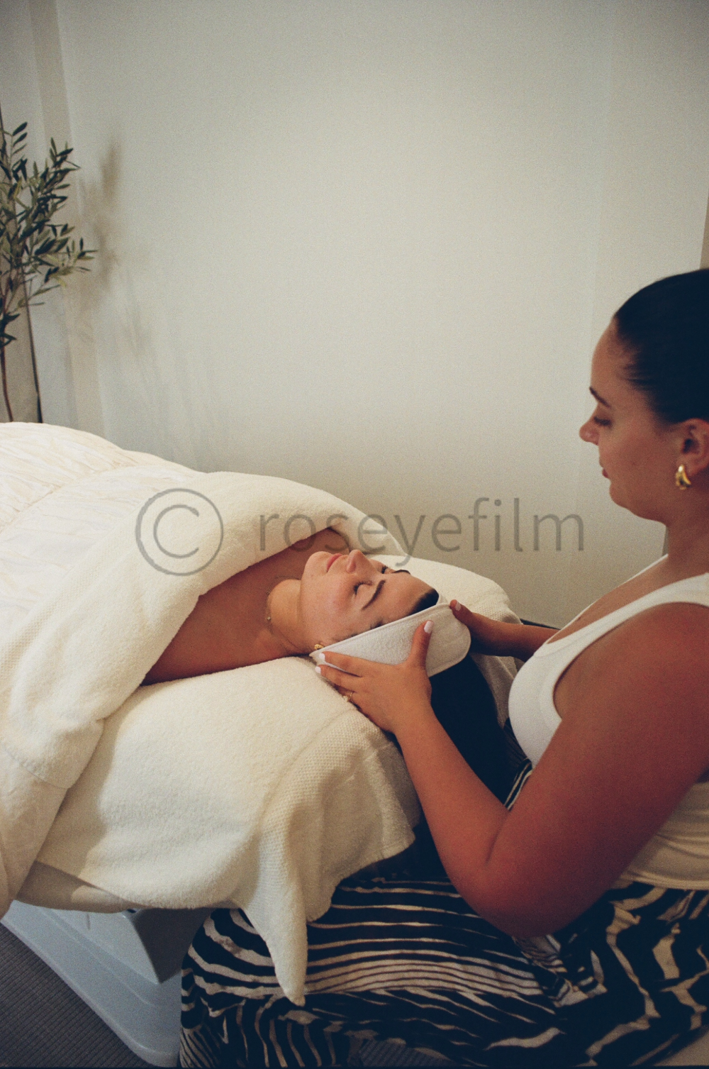 A woman receiving a facial treatment from an esthetician in a spa or skincare clinic.