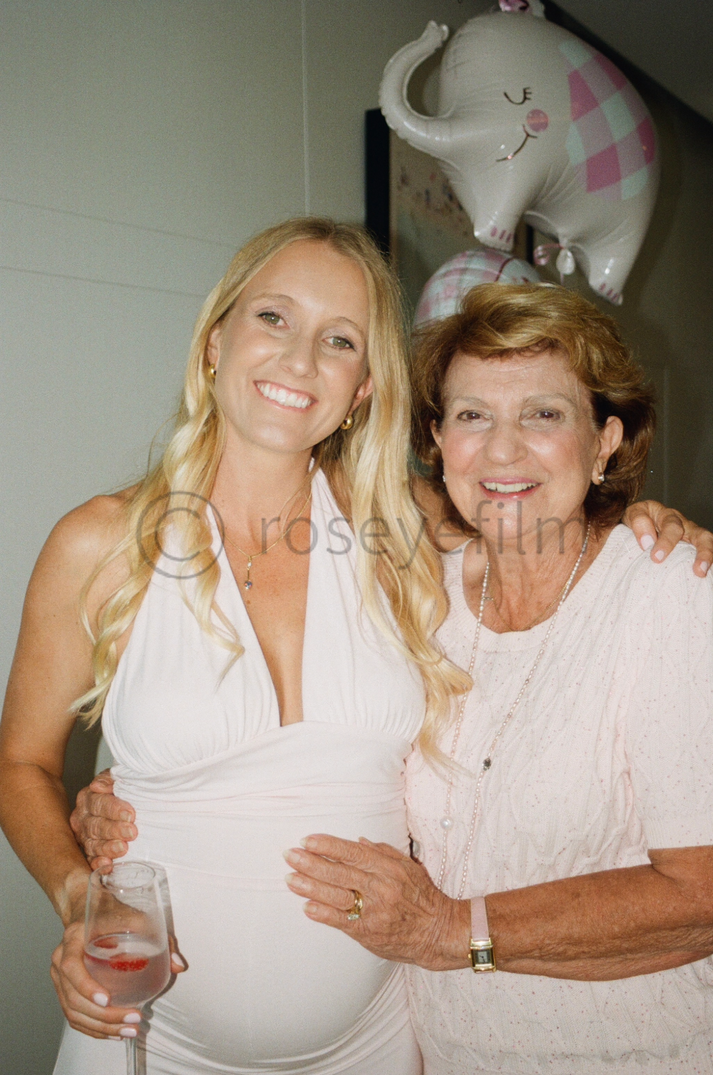 Two women, one pregnant, smiling and posing for a photo at a celebration, with an elephant-shaped balloon in the background.