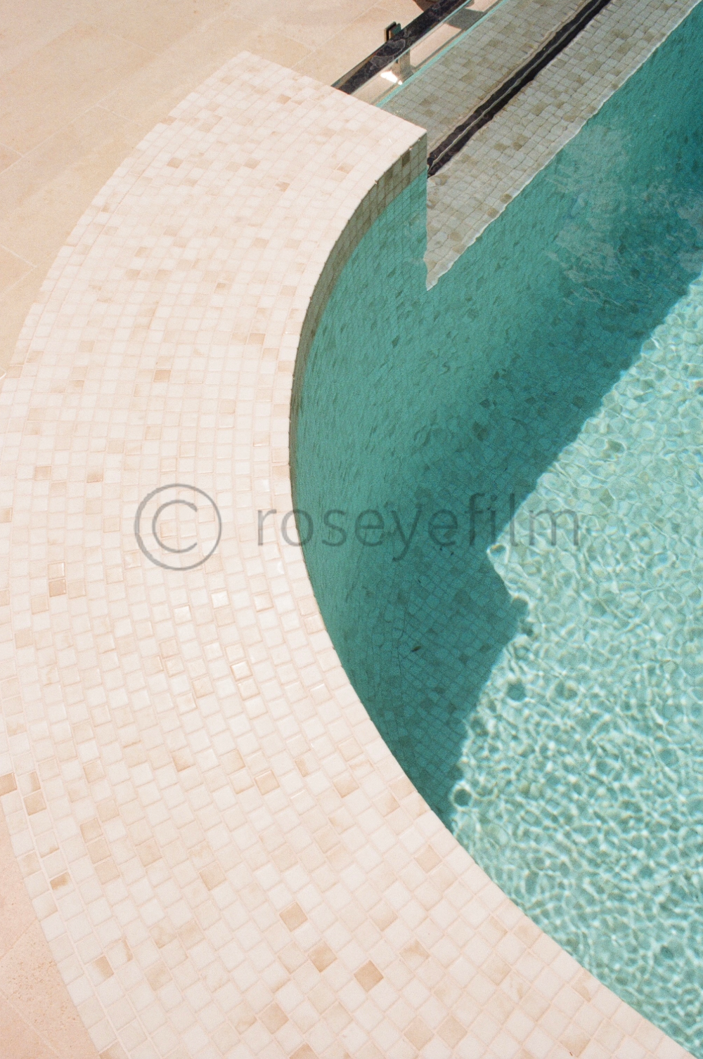 Close-up of a curved, tiled edge of a swimming pool with clear blue water.