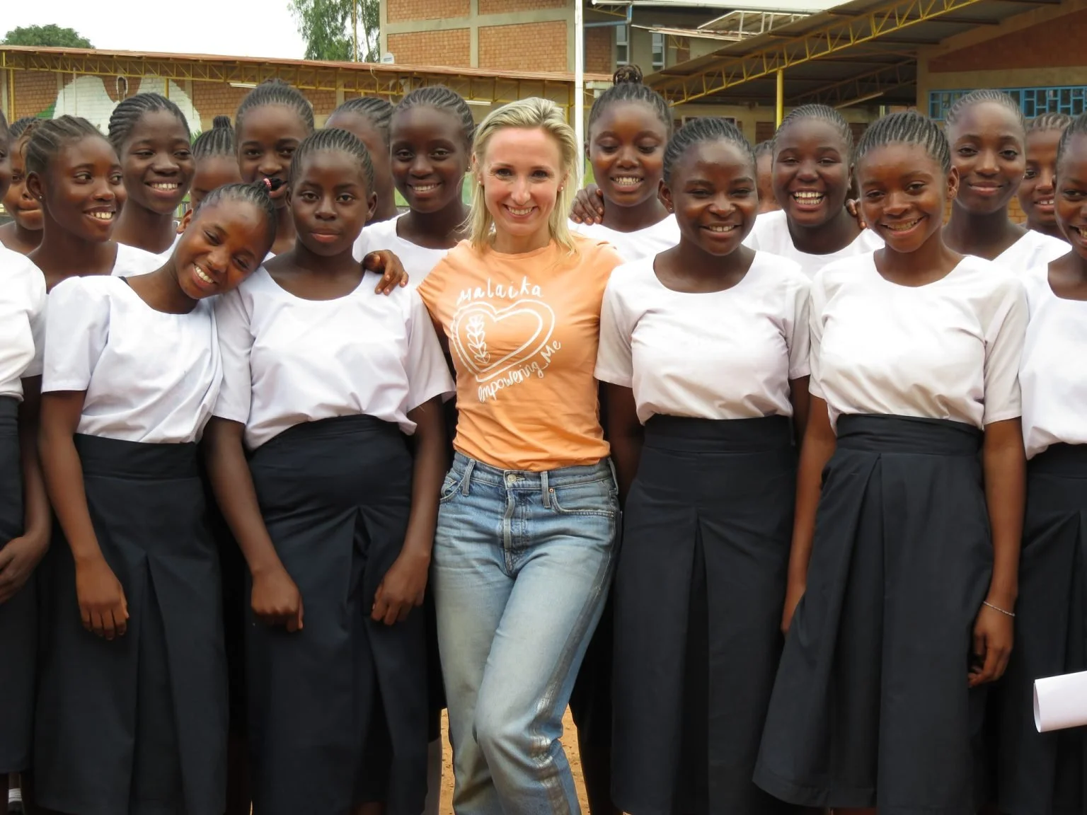 Marta Reed smiling at the camera with a lot of schoolgirls who are also laughing into the camera.