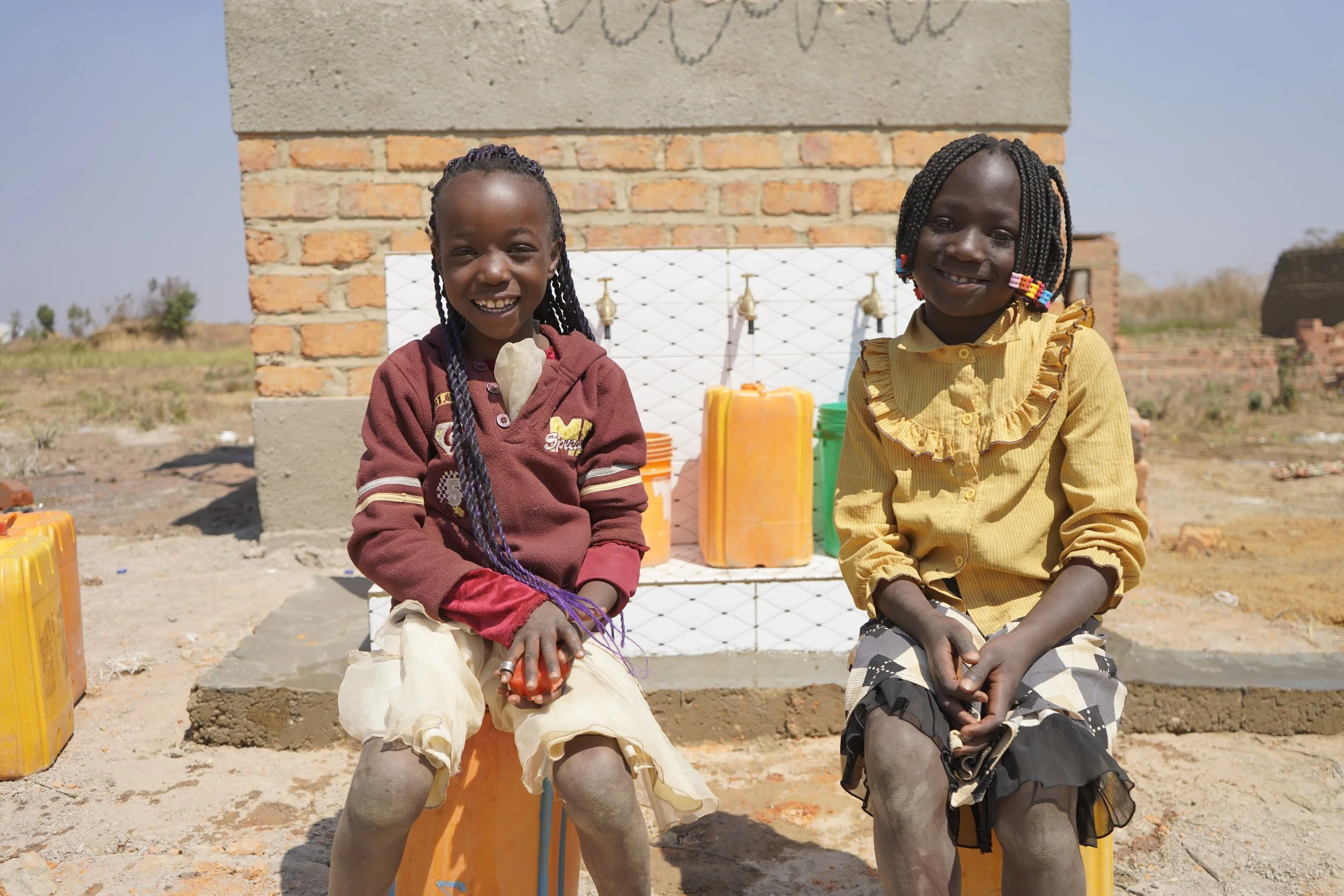 Founder of Malaika with local children around a well. 