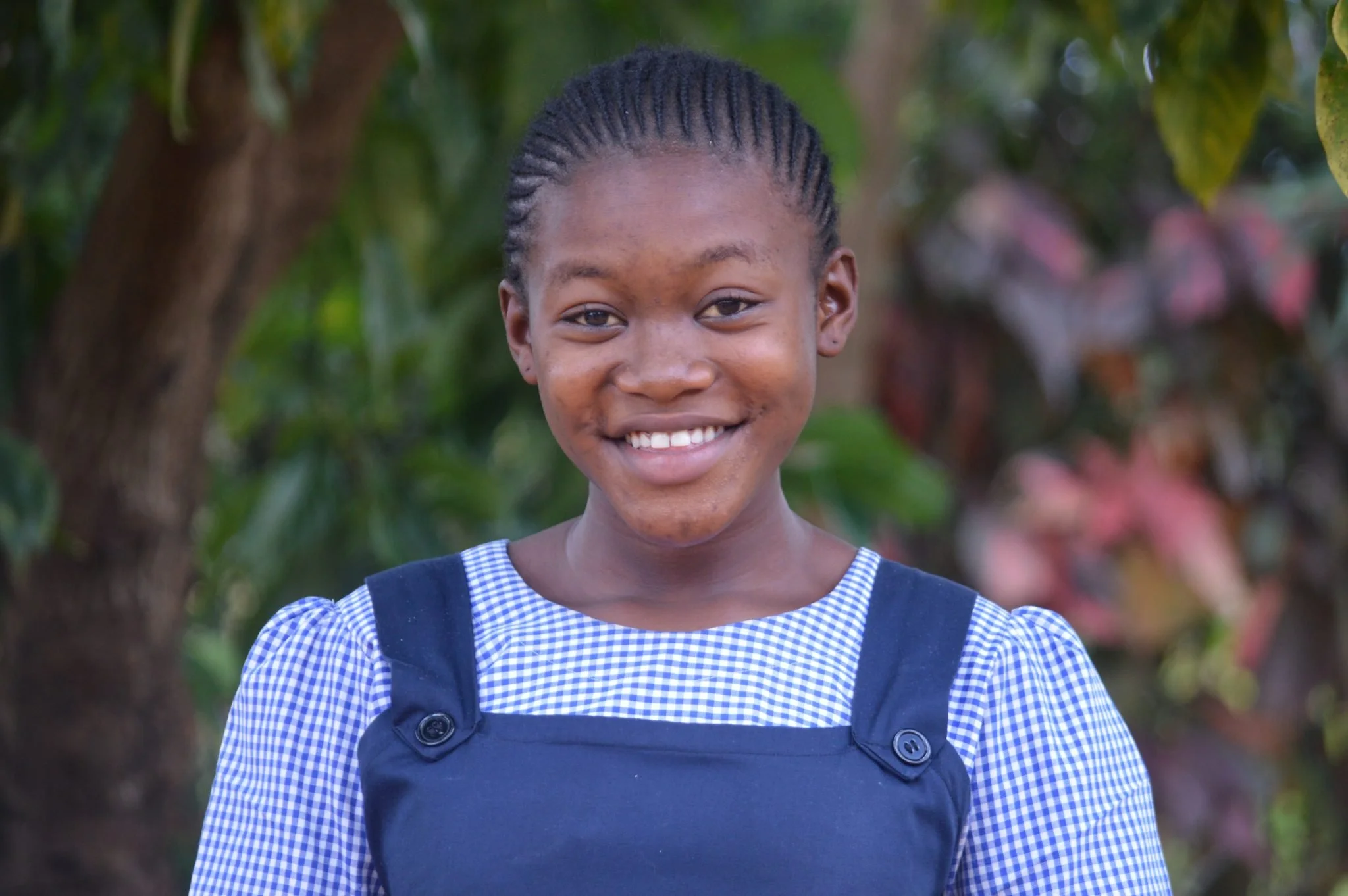 Kessia wearing a blue shirt and smiling at the camera with a tree in the background.