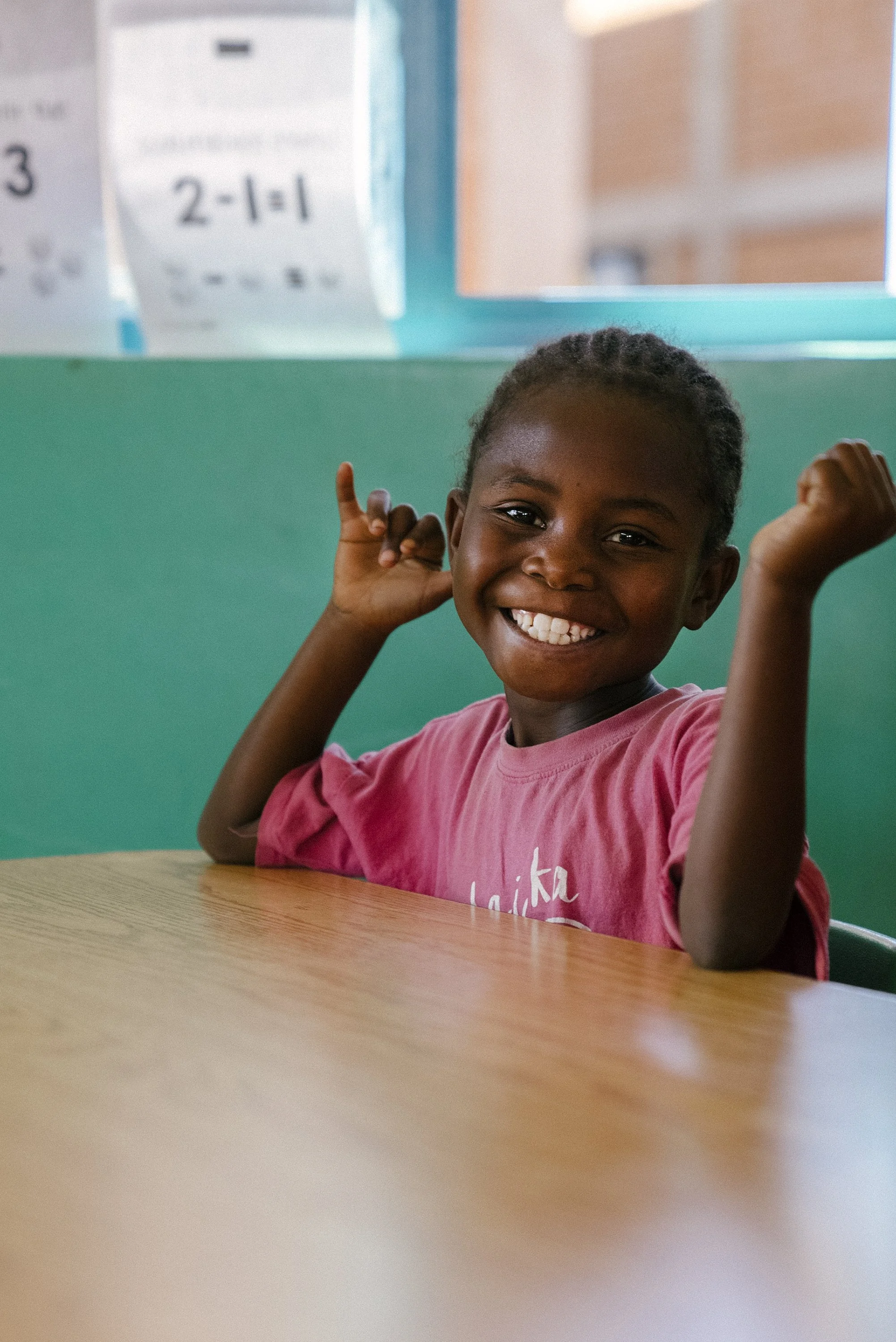 Cute, young schoolgirl from Congo smiling and sitting at a table. 