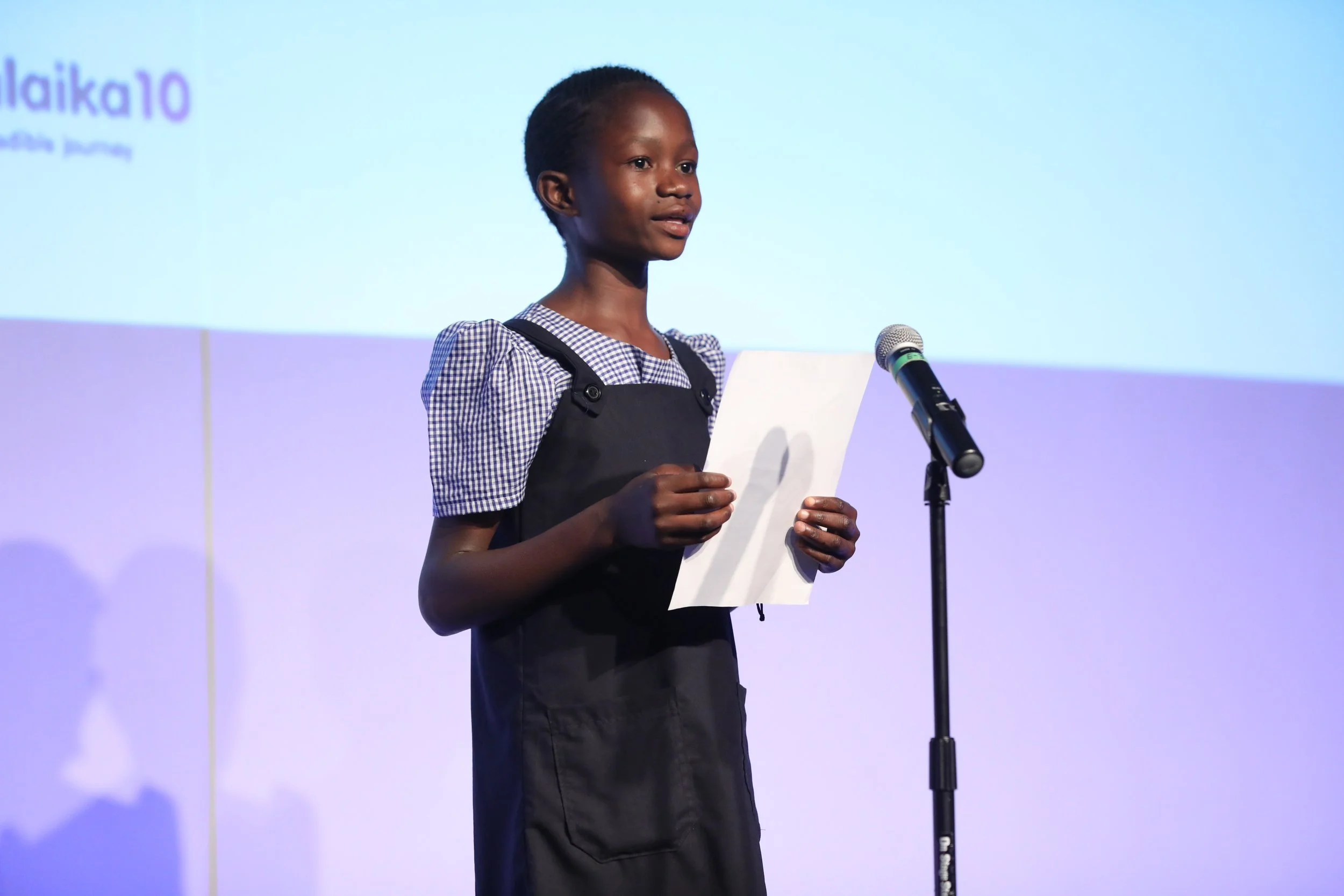 Louise at the age of six on a stage in New York City at the Malaika 10-year anniversary with a piece of paper in her hand.