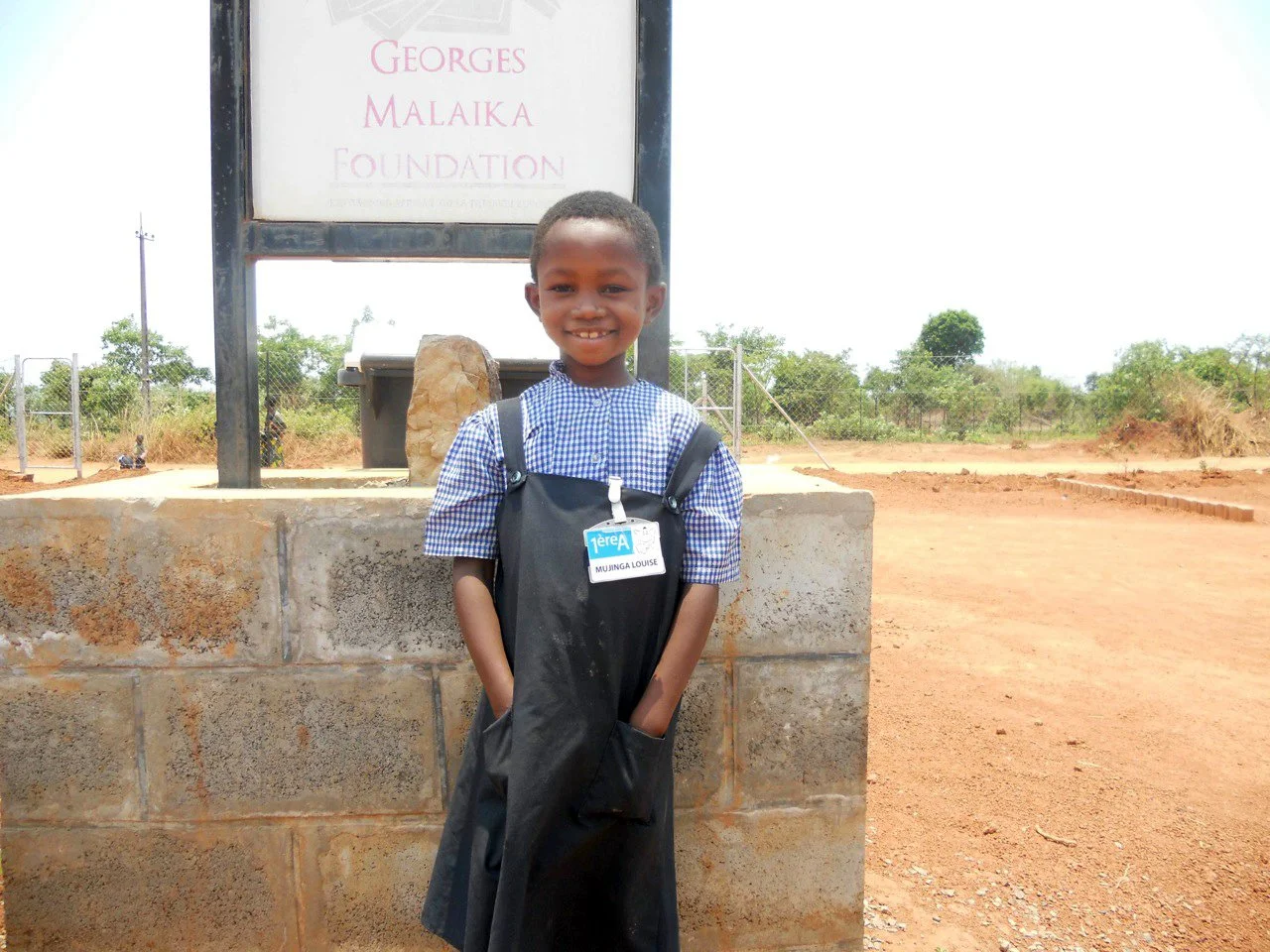 Malaika student Louise at the age of 5 in front of the Georges Malaika Foundation sign.