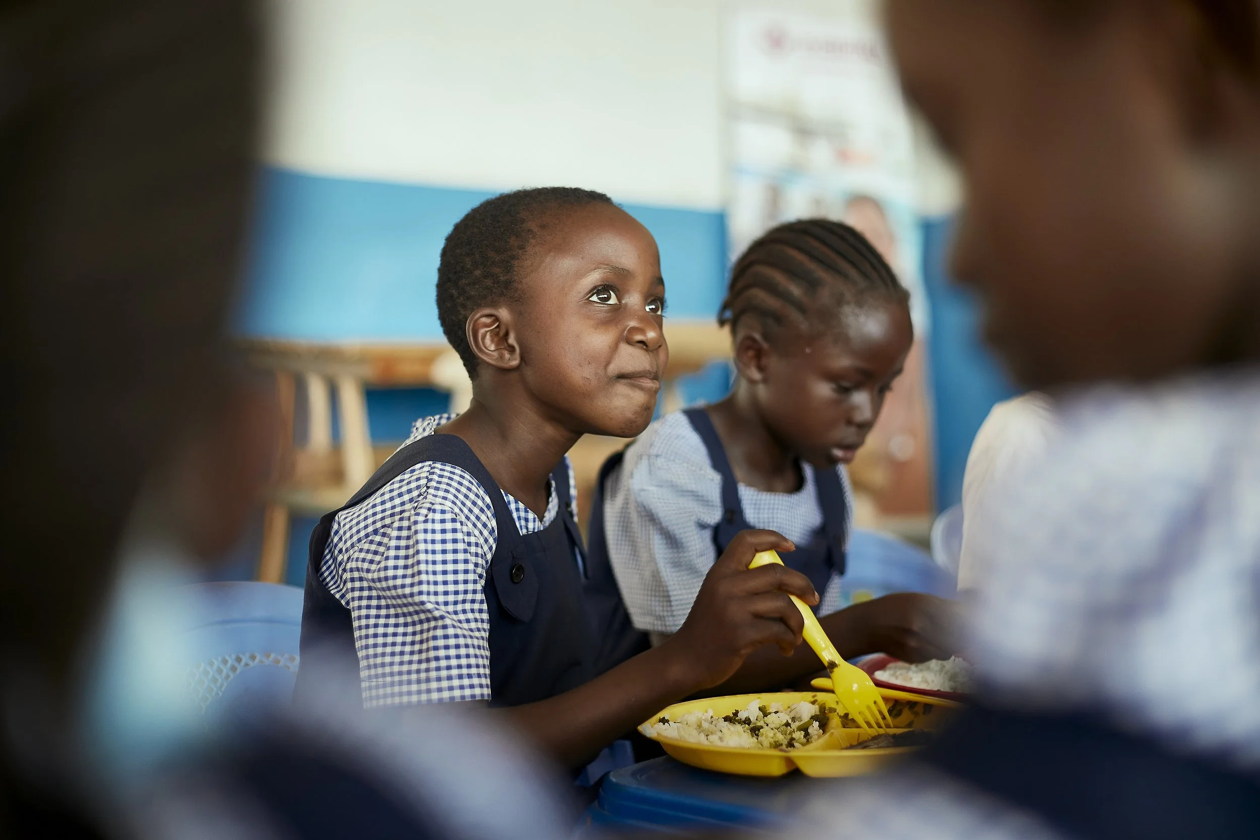 Young schoolgirl sitting in the cantine with a plate of freshly prepared food. She is holding her spoon looking in the distance with a pleased look on her face. 