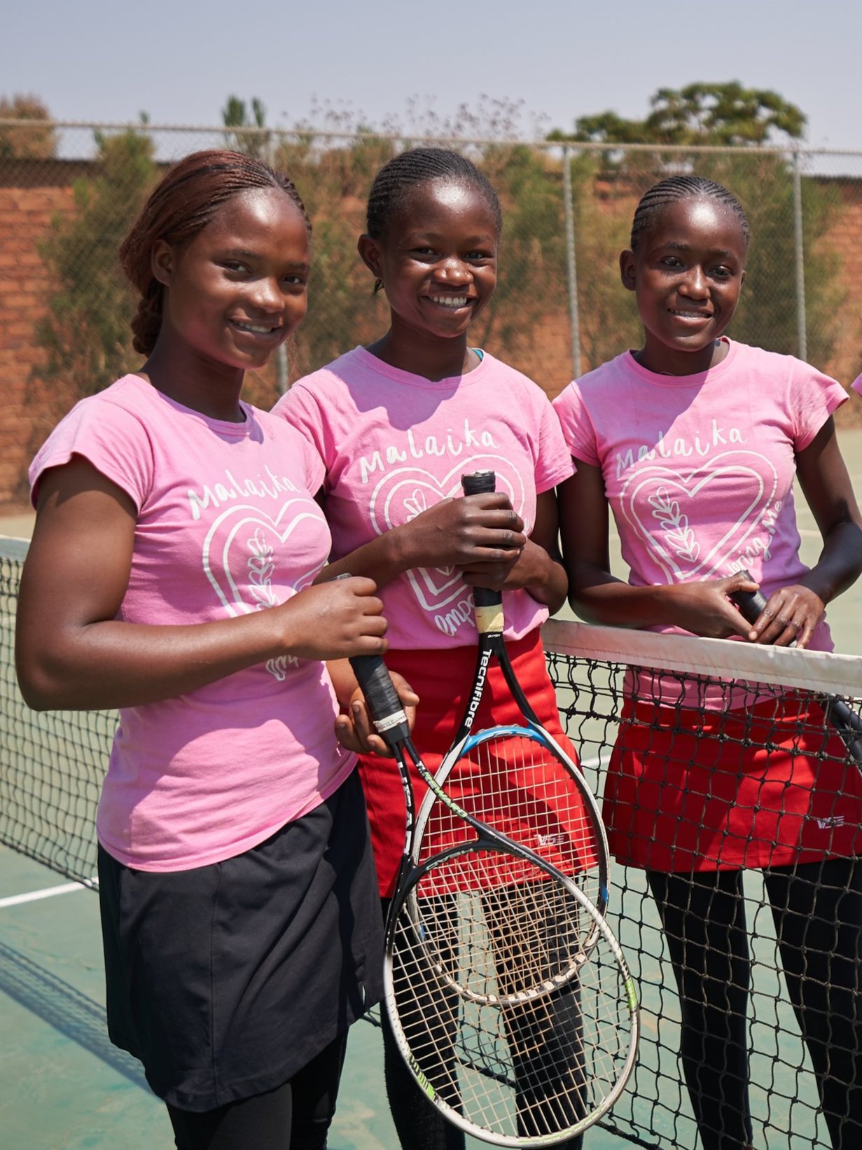 Louise with other Malaika students on the tennis court smiling at the camera.