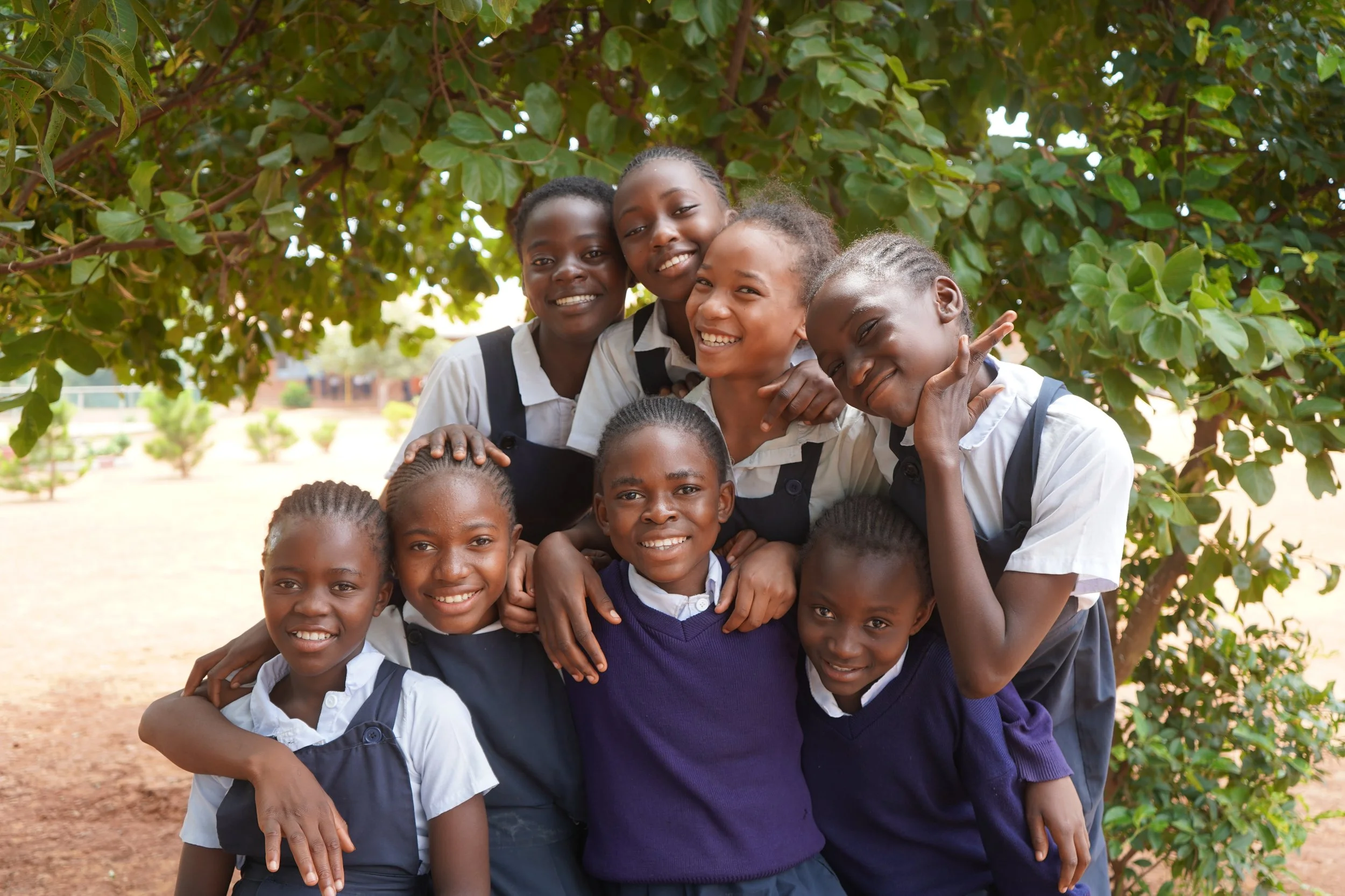 Eight schoolgirls smiling and holding each other.