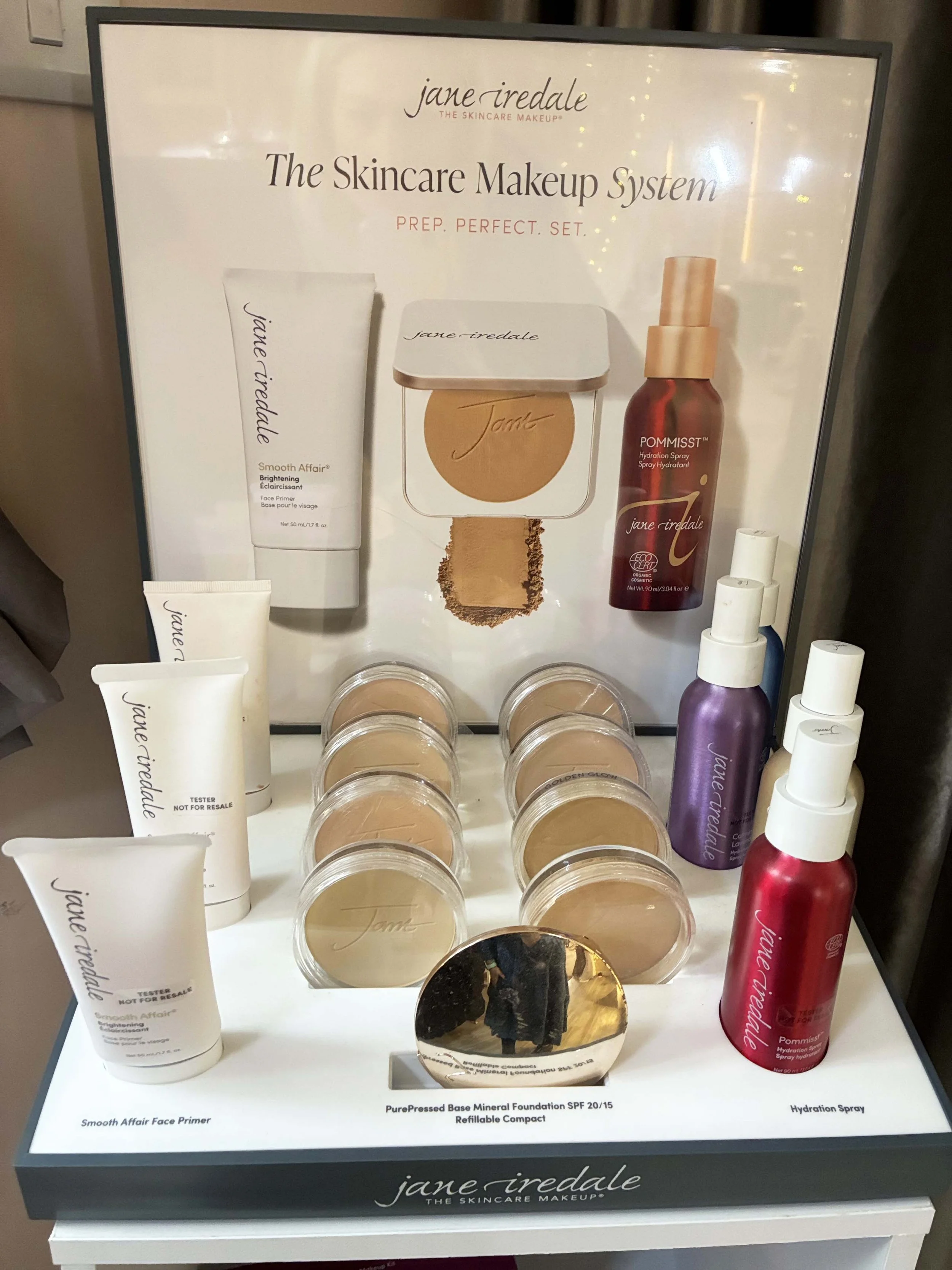 Display of Jane Iredale skincare makeup products, including face primer, foundation, moisturizing sprays, and powders, with branding and product details.