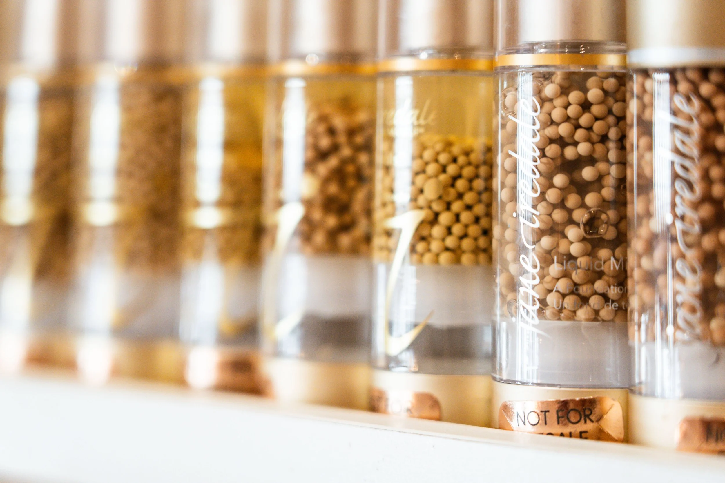 Row of clear spice bottles filled with different spices on a shelf.