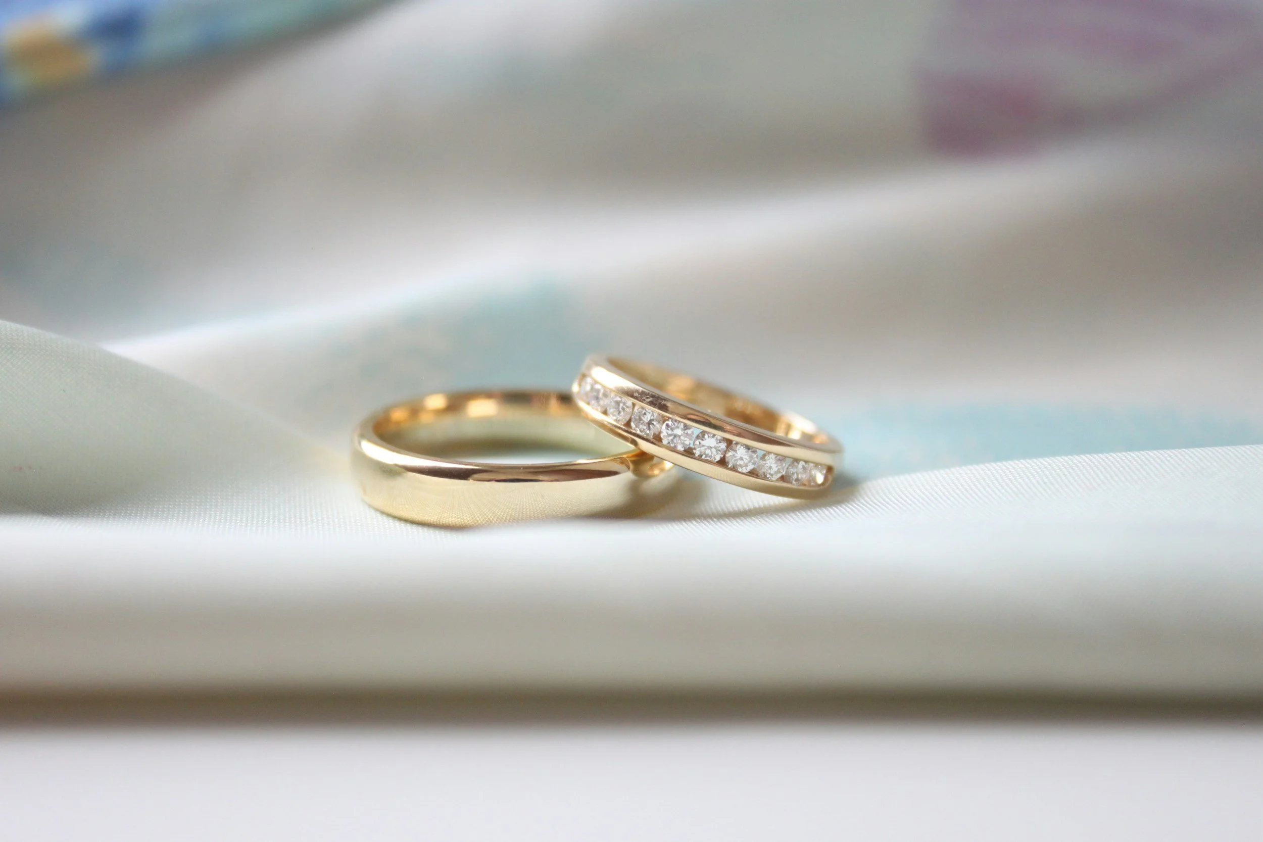 Two gold rings with embedded diamonds resting on a silky white fabric.