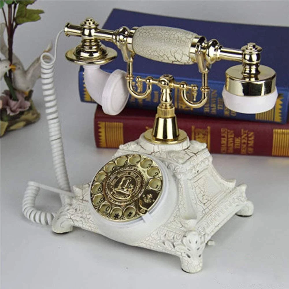 Decorative vintage rotary telephone with a gold and white ornate base, placed on a desk with hardcover books in the background.