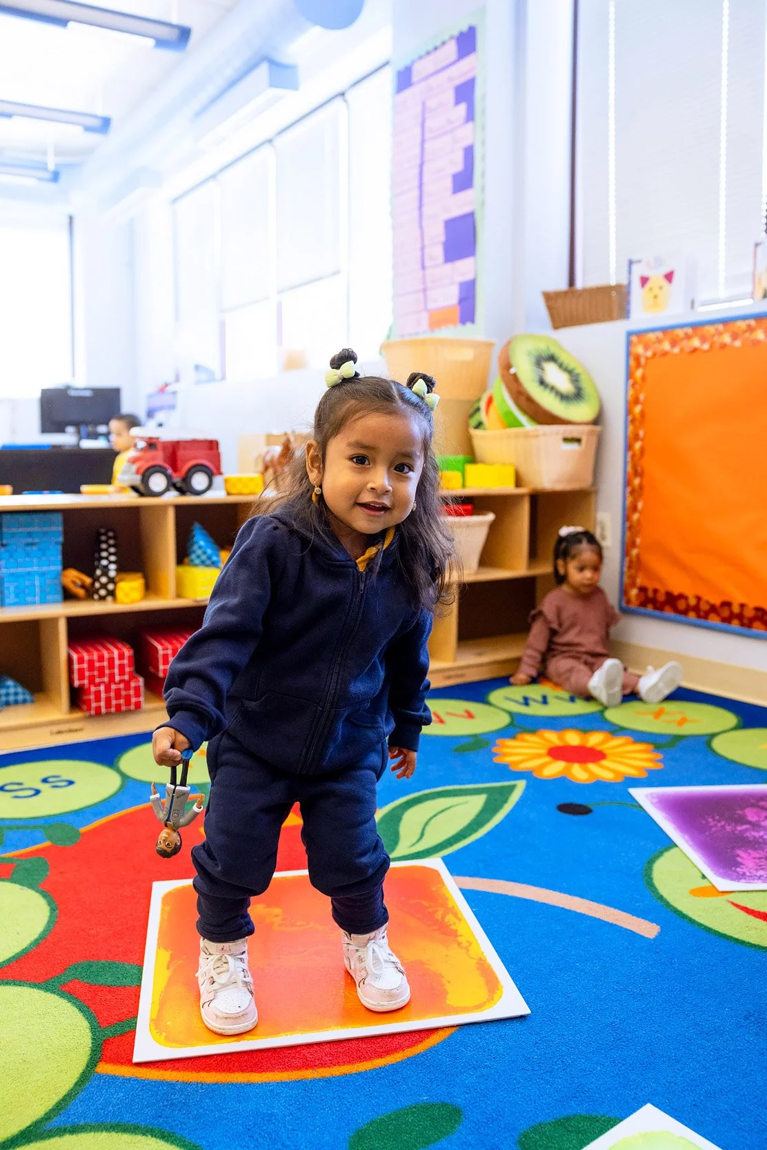 Young child standing on colorful classroom carpet during play-based learning activity.
