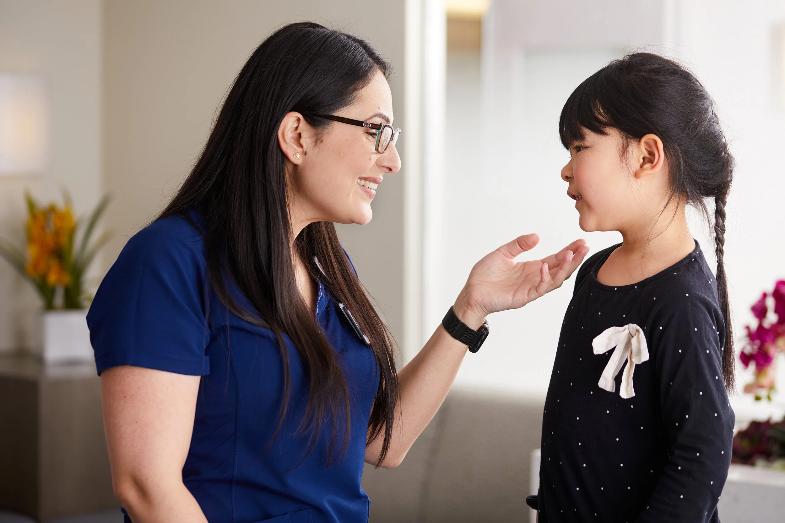 Nurse in dark blue scrubs comforting a young girl in a clinical setting.