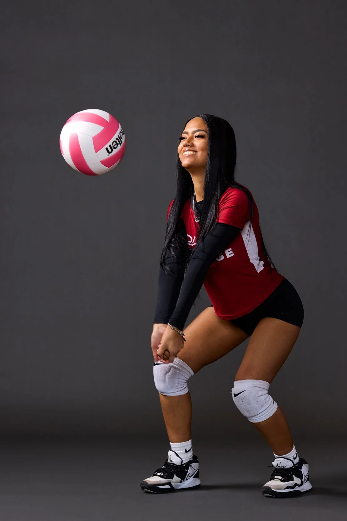 Student athlete in uniform posing with volleyball against dark studio background.