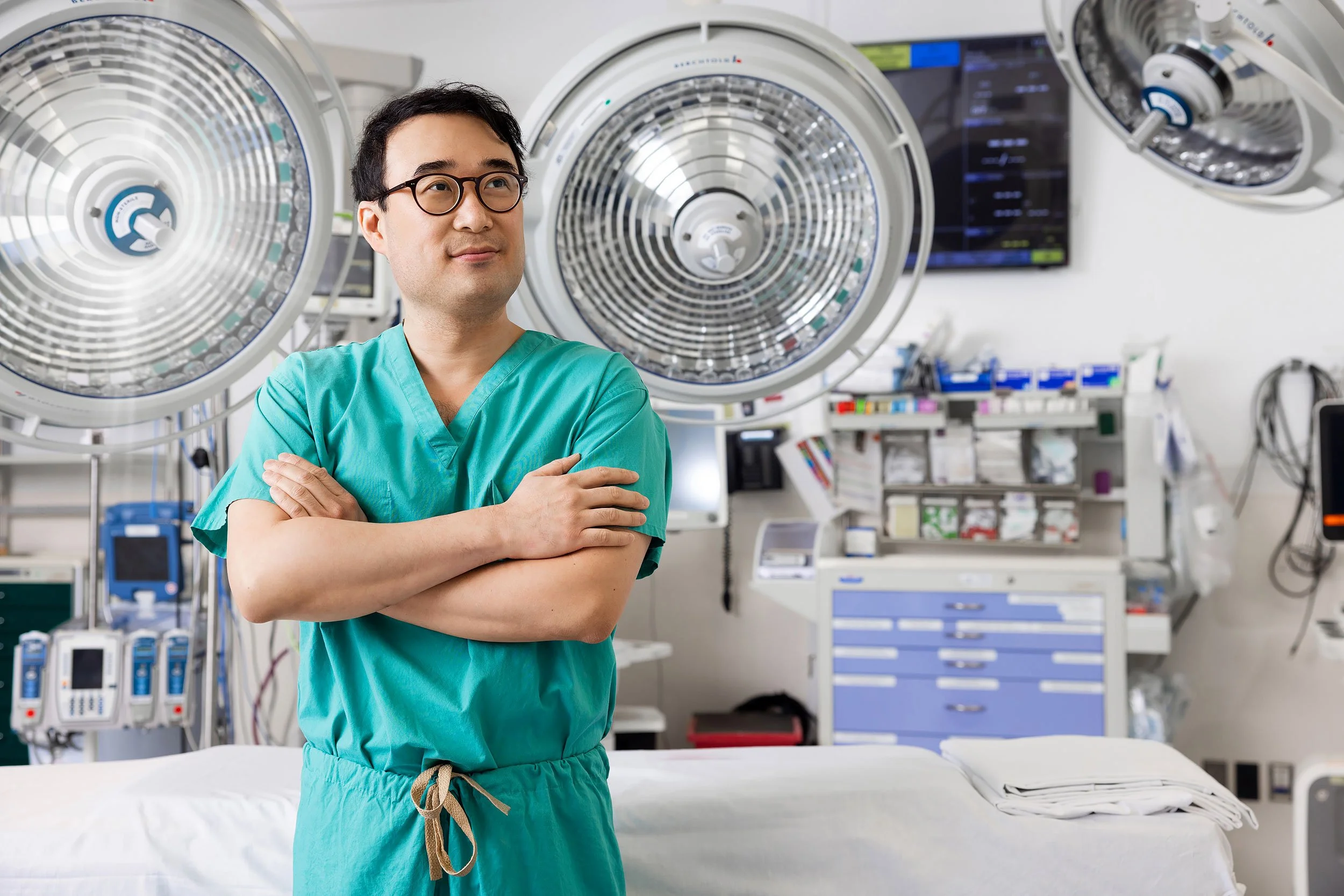 Doctor in green scrubs with arms crossed in an operating room looking away from the camera.