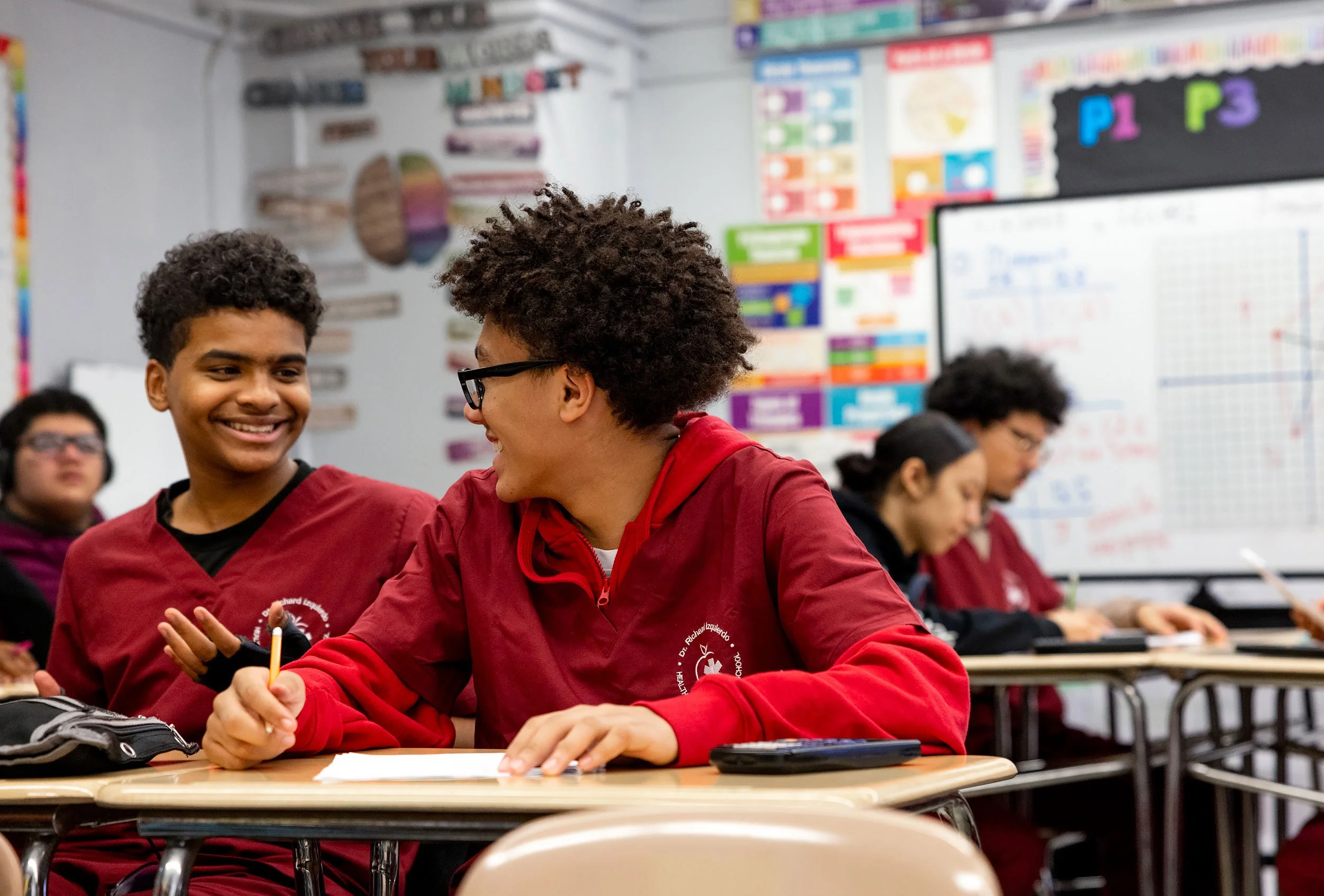 Two students sitting together at table engaged in conversation during class.