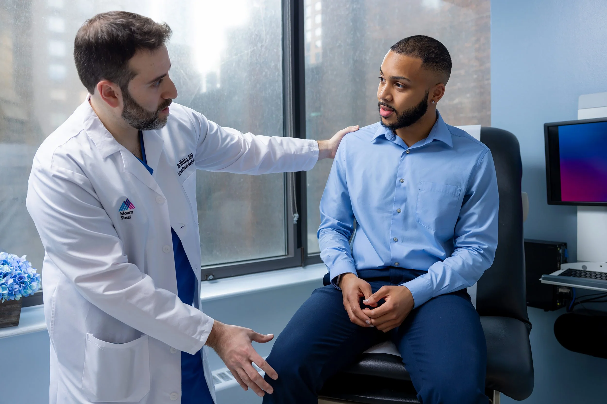 Male doctor examining a male patient’s knee in a clinical office.