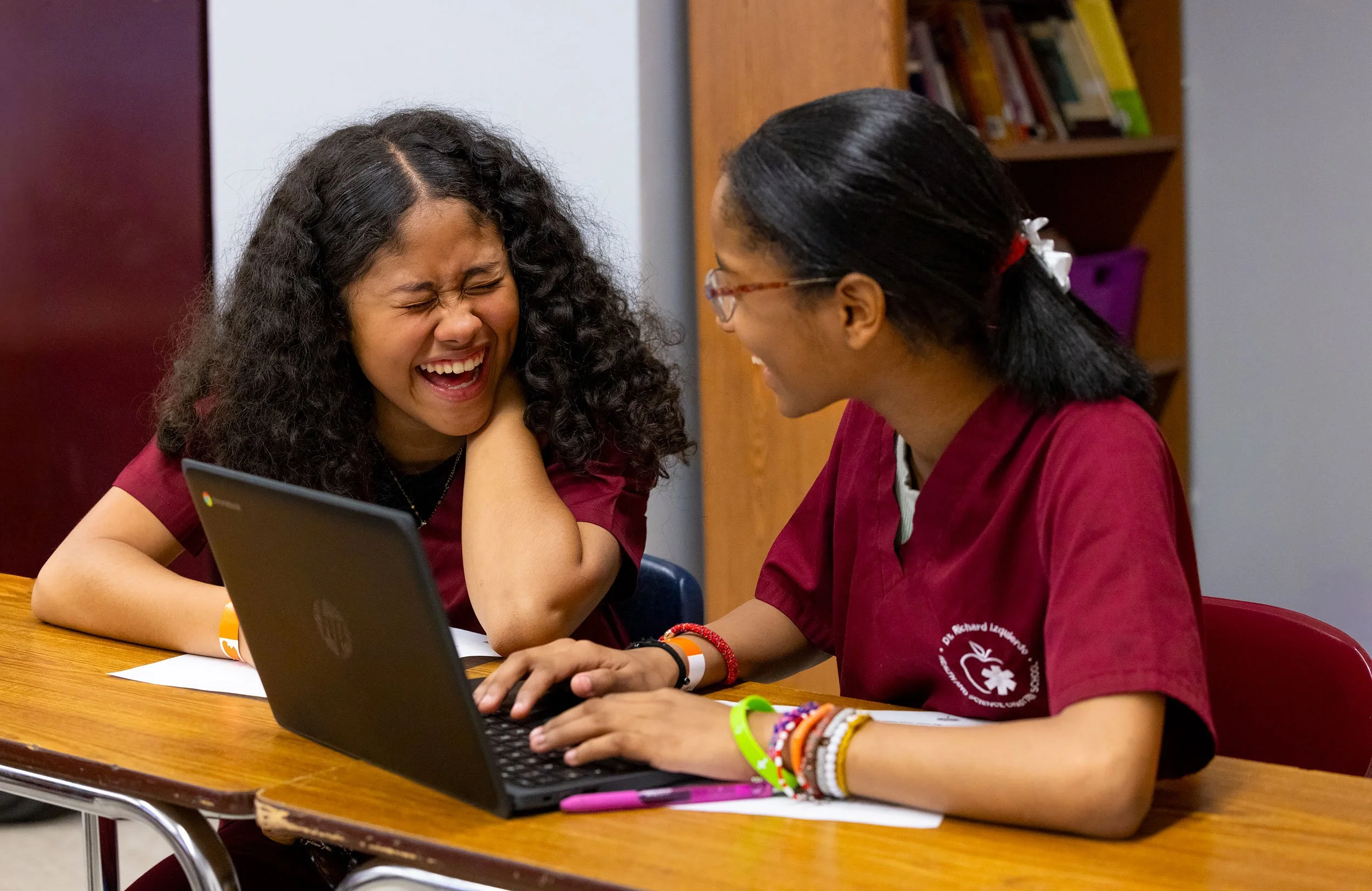 Two students collaborating on laptop project in classroom setting.
