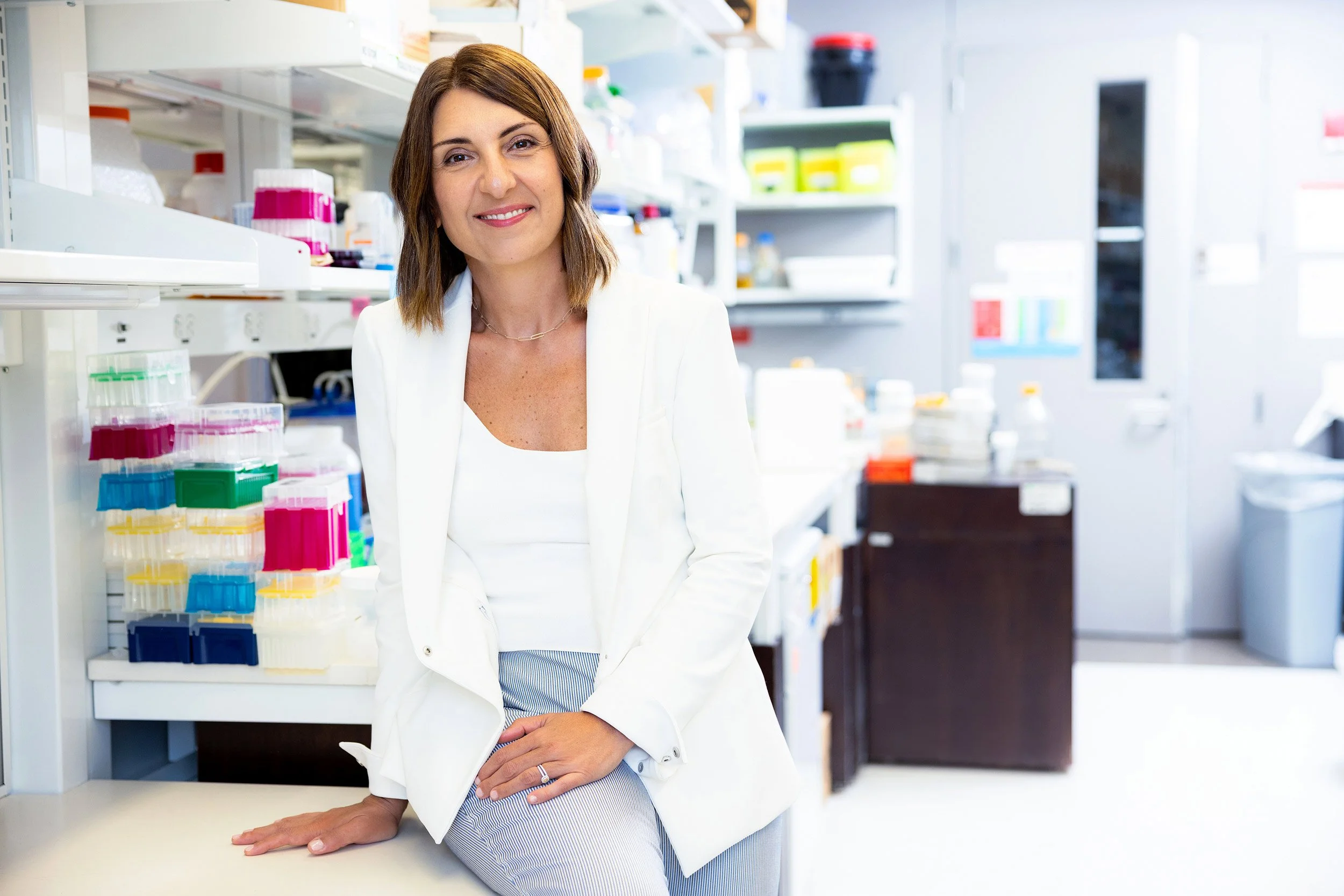 Female scientist in white coat smiling in her research lab.