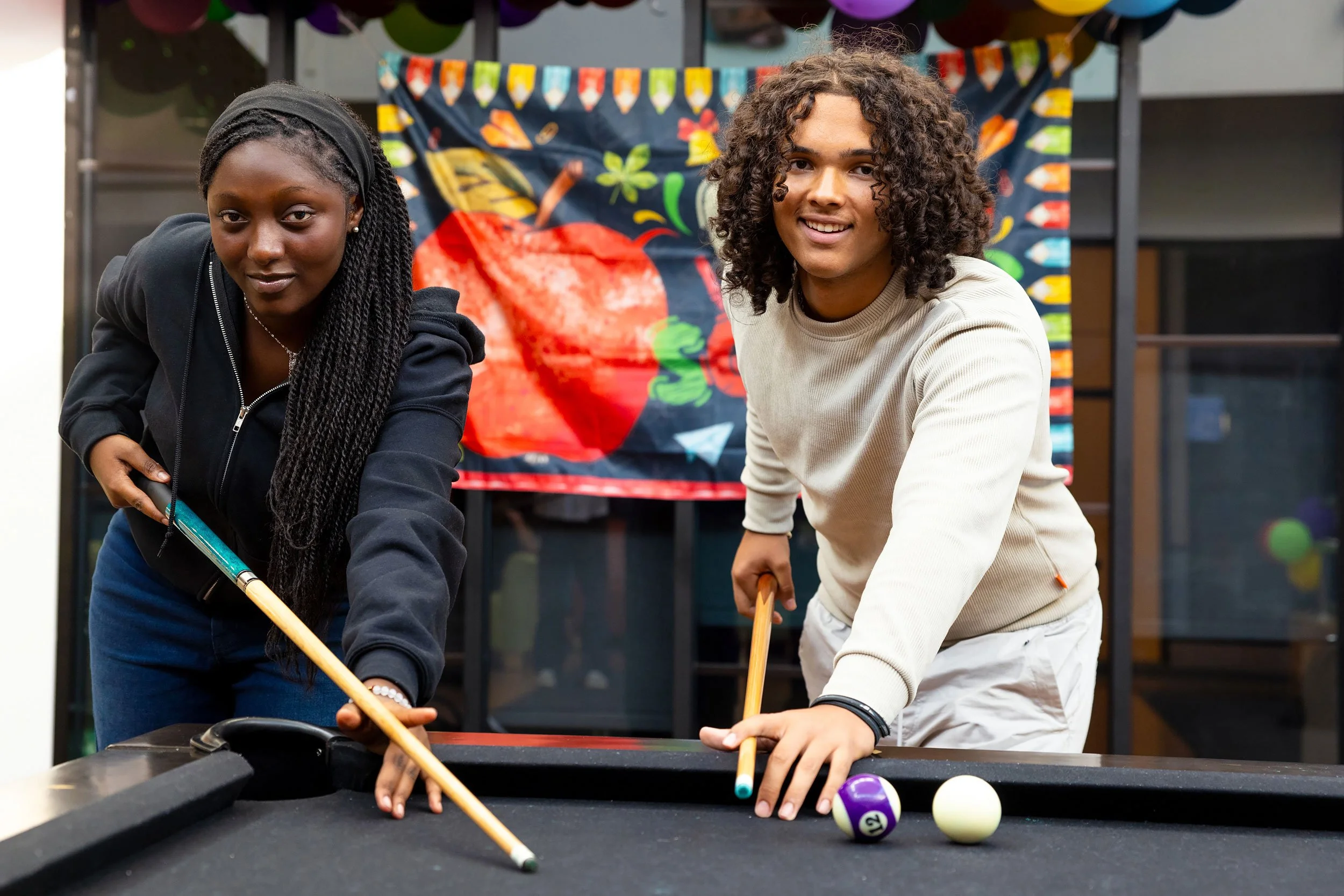 Two students playing pool together in a school recreation space.
