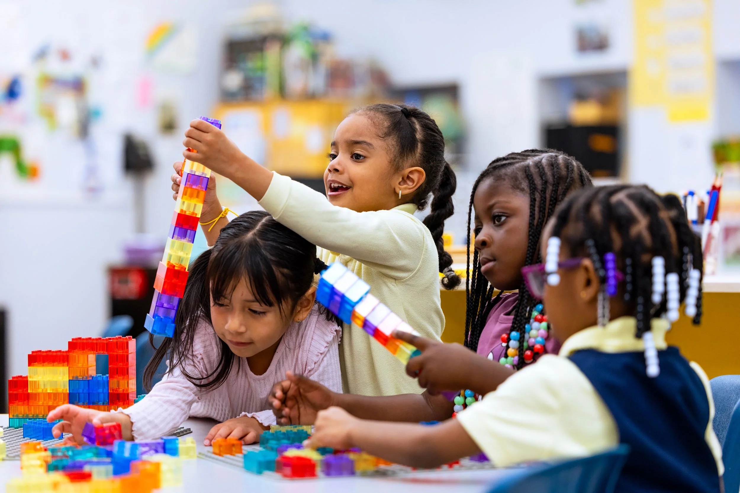 Group of young girls building with colorful blocks during classroom playtime.