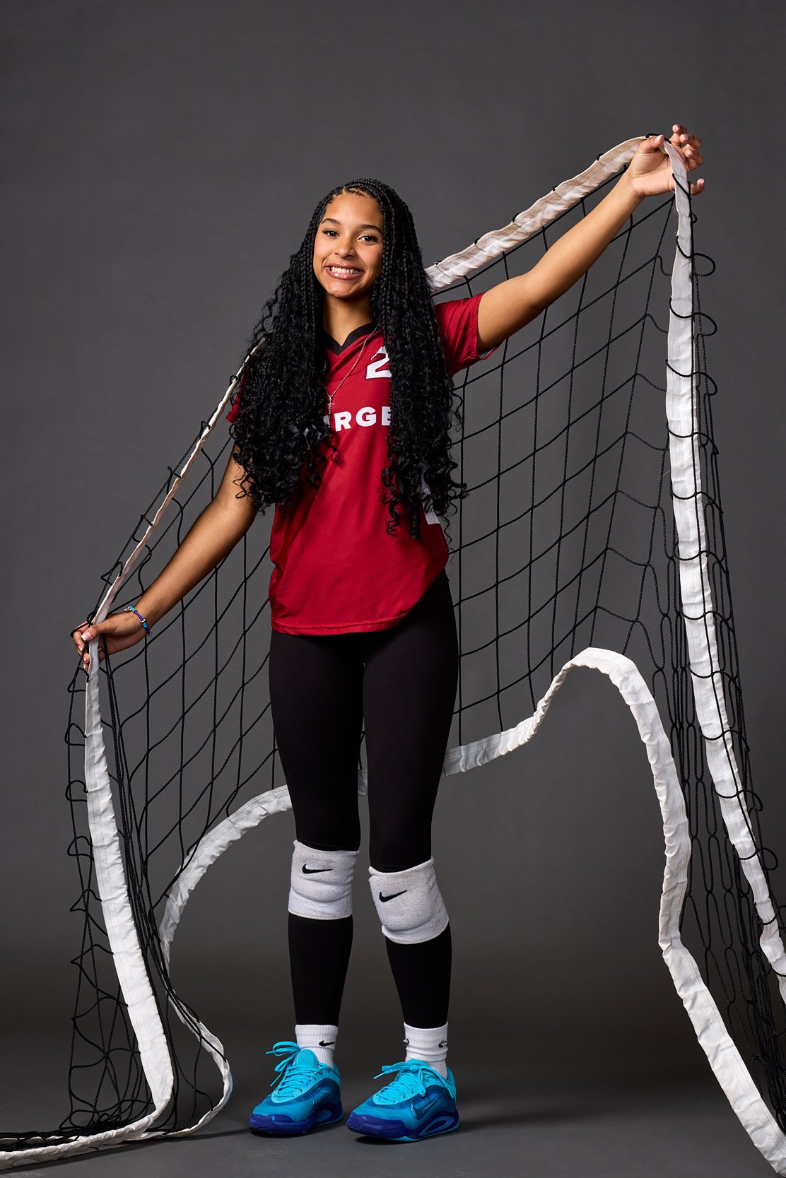 Student athlete holding volleyball net in studio setting.