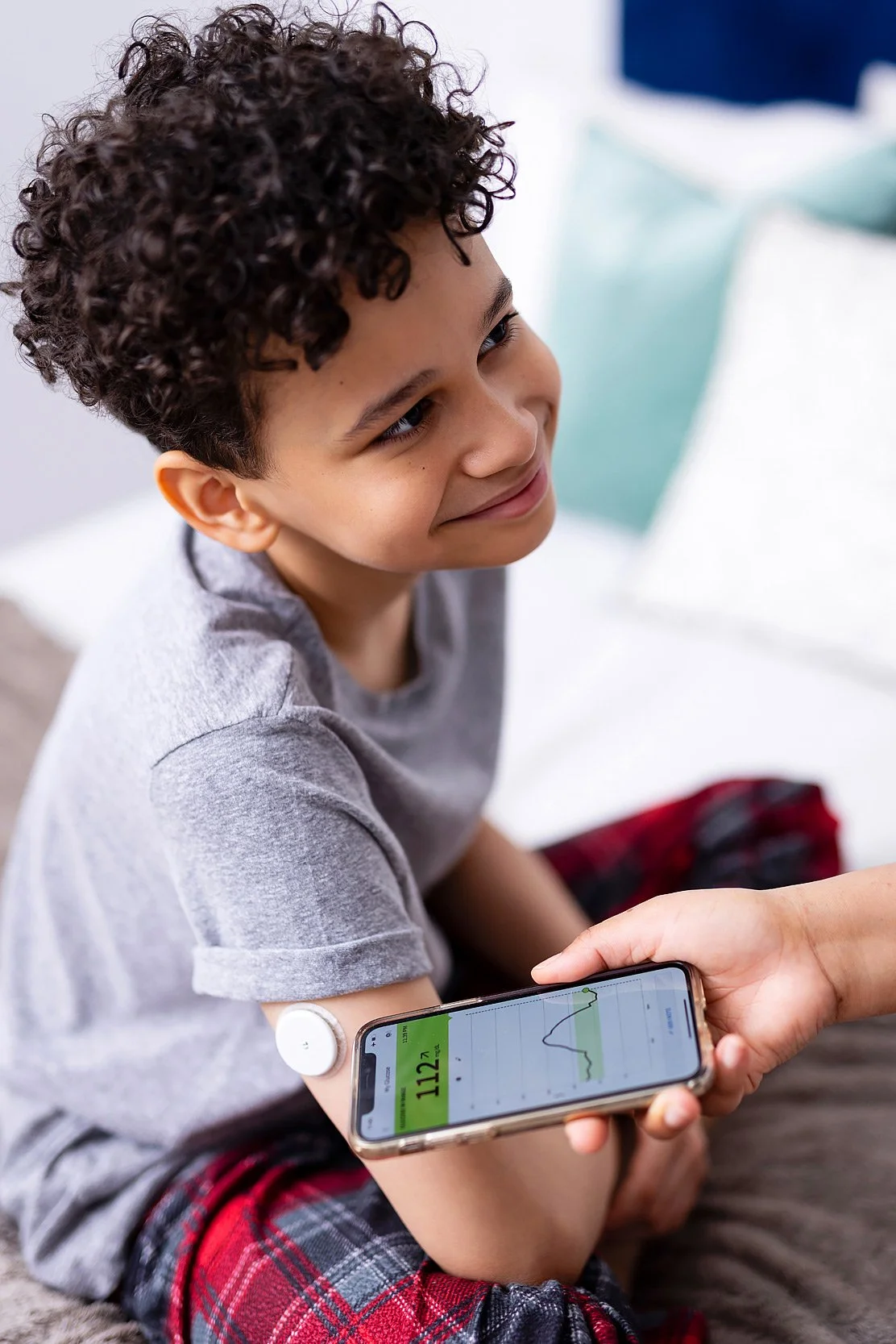 Young boy smiling while someone is measuring his blood sugar with a medical device (blood sugar monitor)