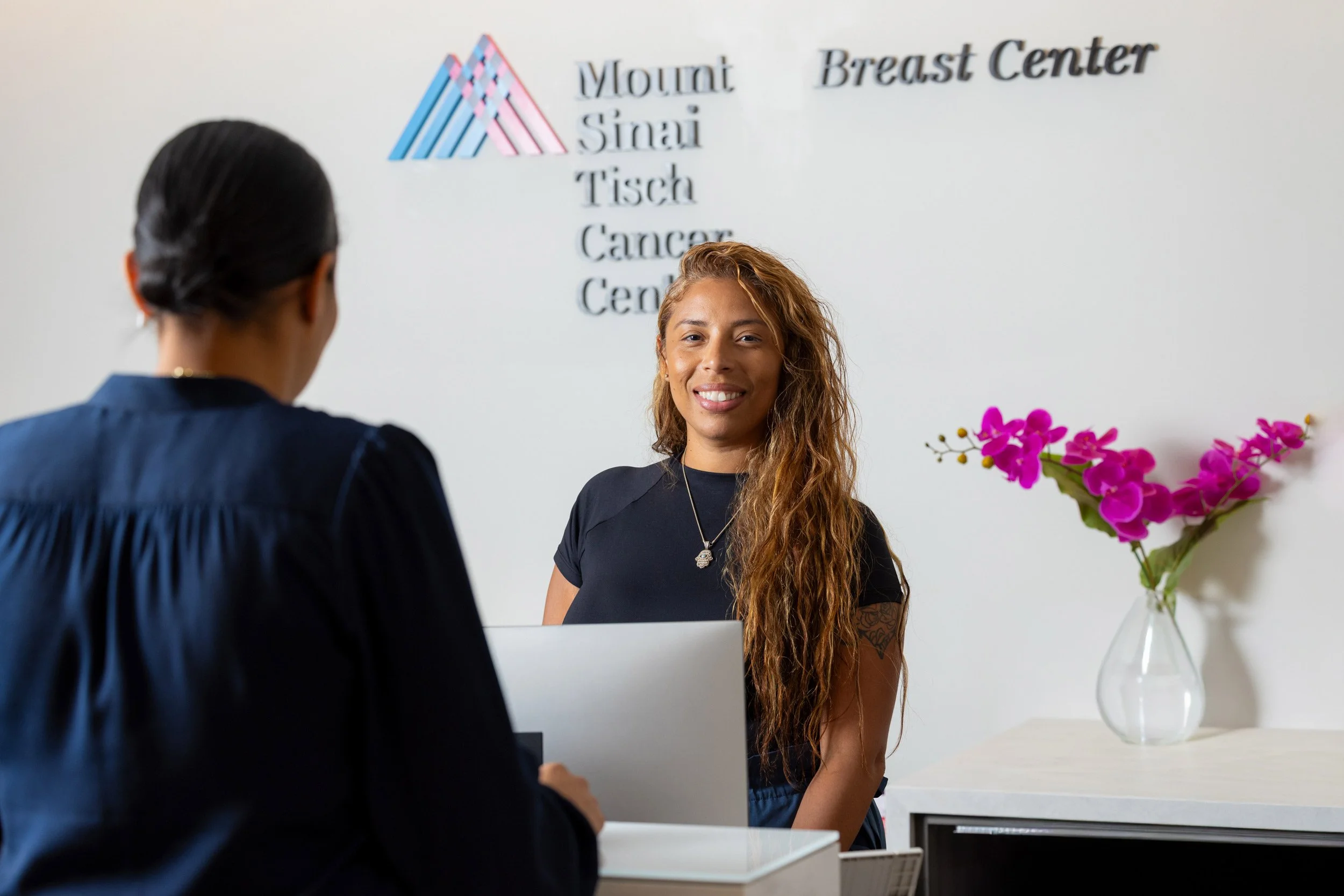 Receptionist greeting a patient at a breast cancer facility's front desk.