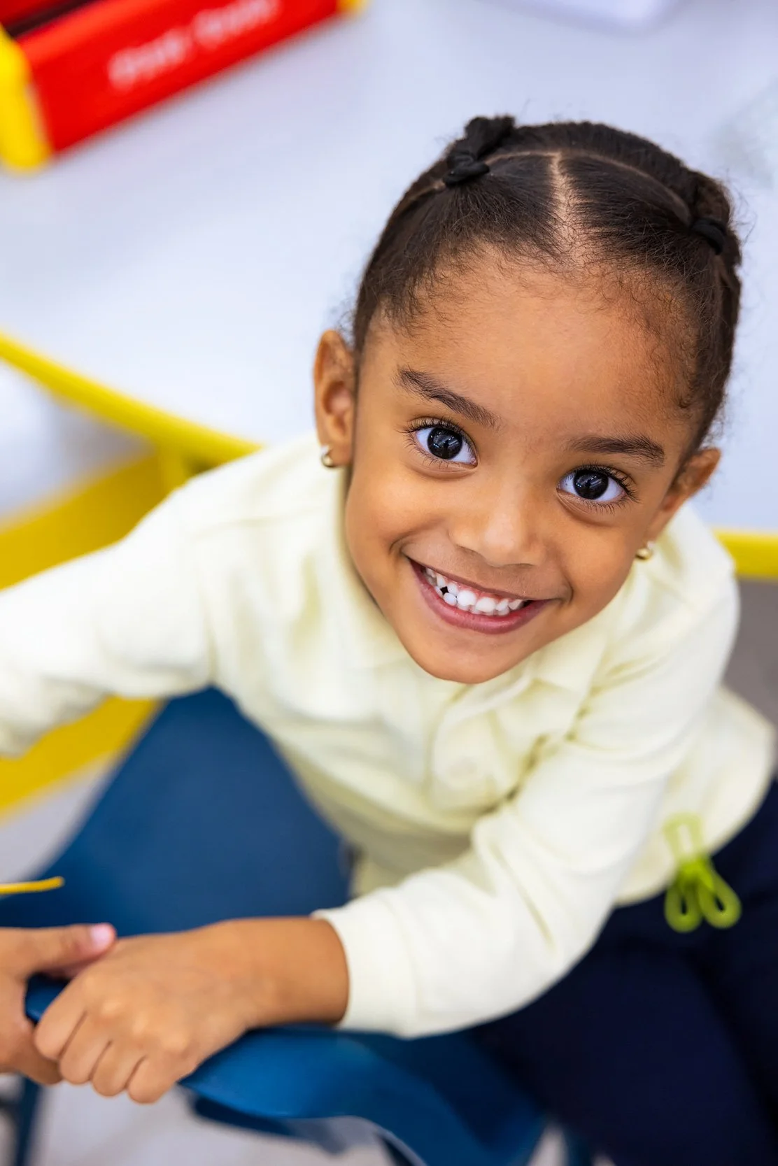 Close-up of smiling young girl leaning on desk in a brightly lit environment. 
