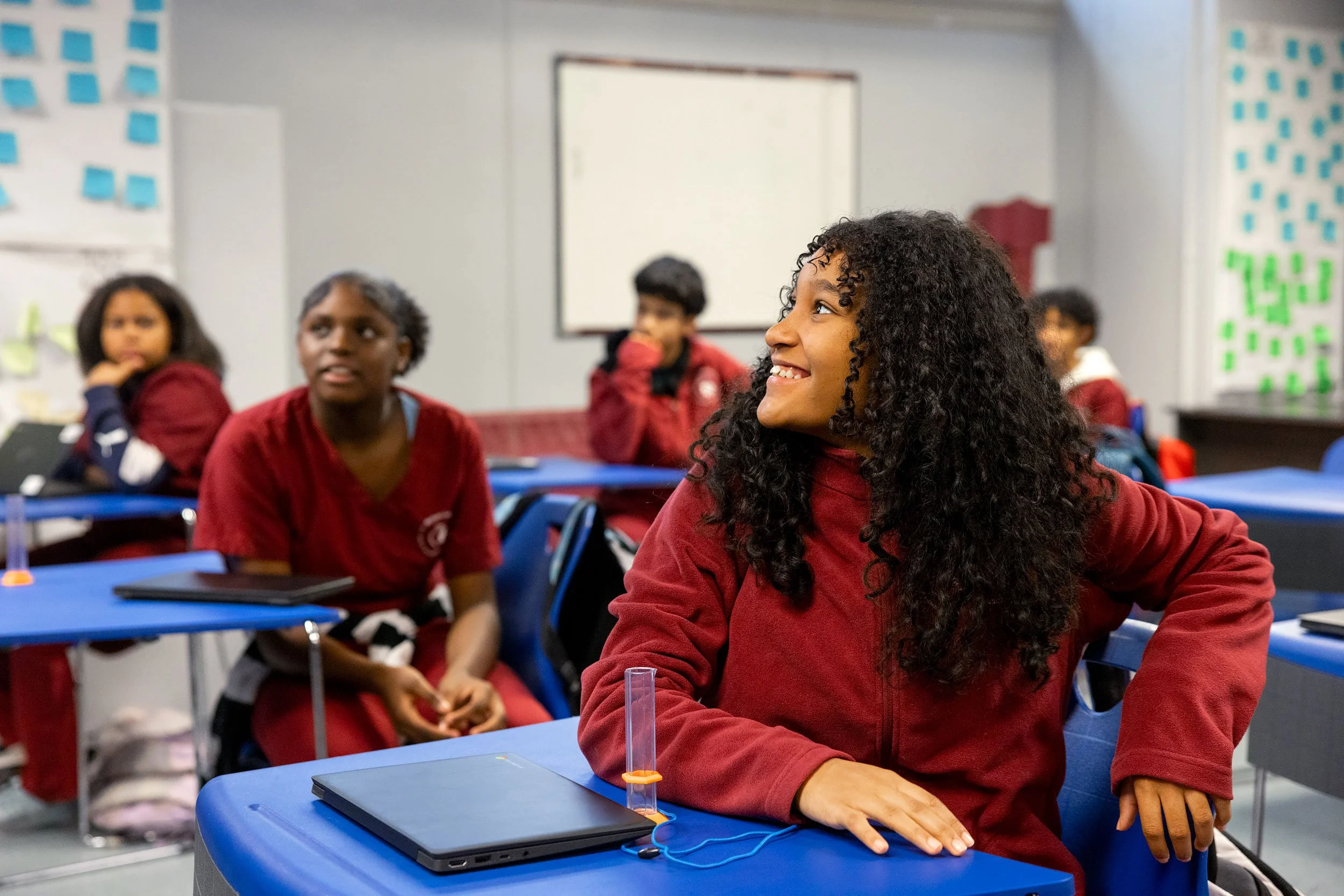 Students in red uniforms seated together in classroom listening attentively to lesson.
