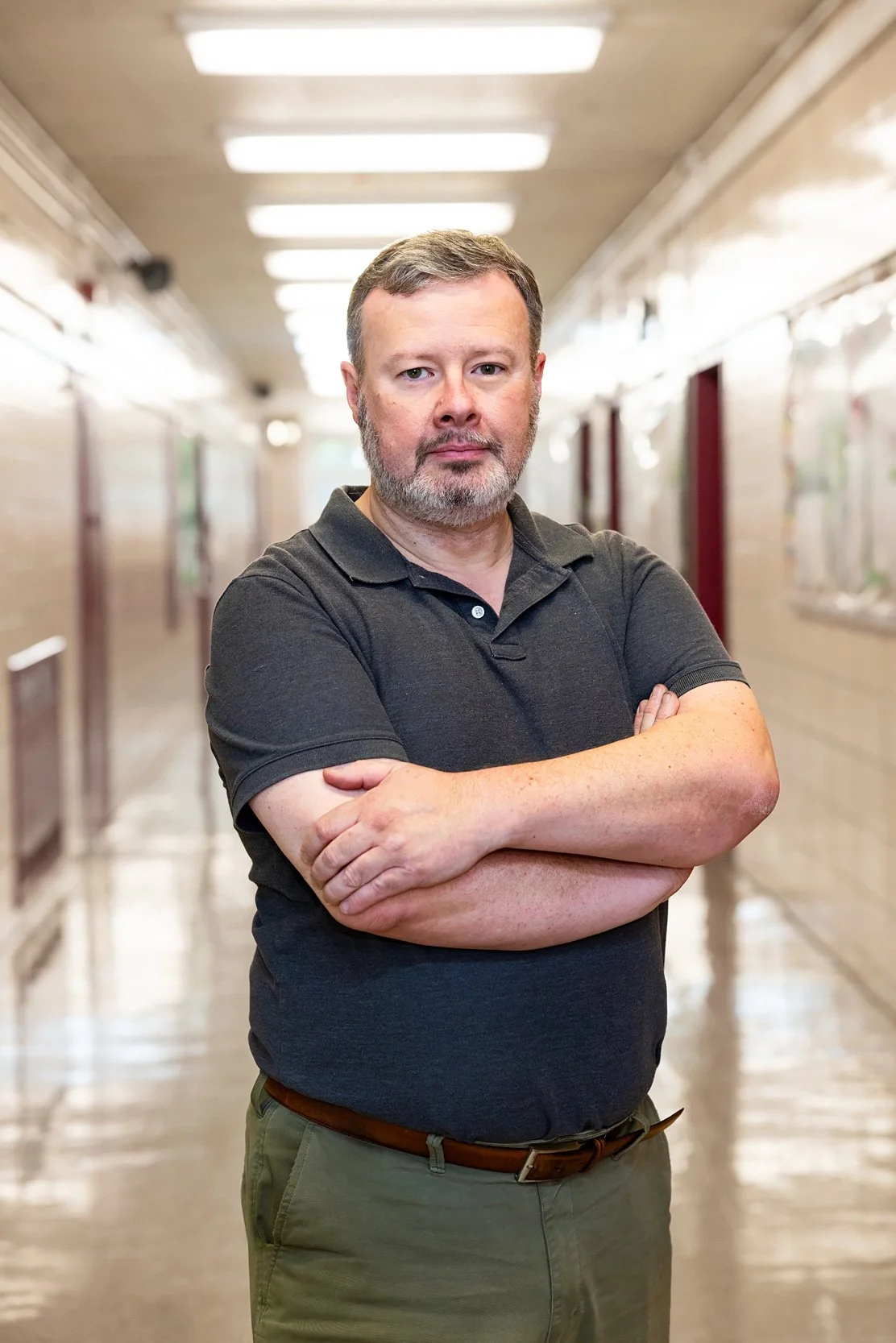 School staff member standing in hallway with arms crossed, portrait-style image.